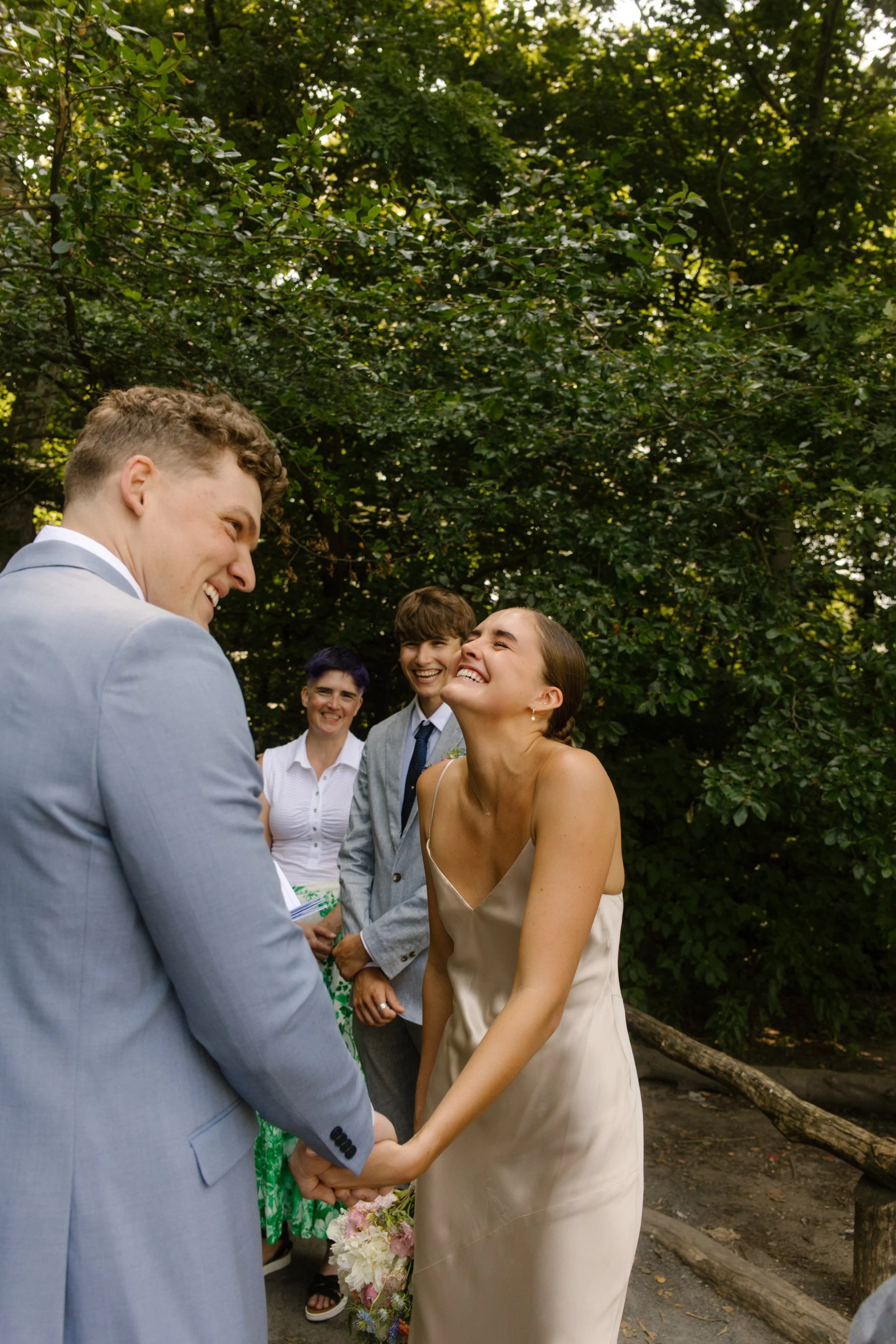 The bride beams up at her groom mid-vow as their families laugh behind them during an intimate elopement ceremony in Central Park.