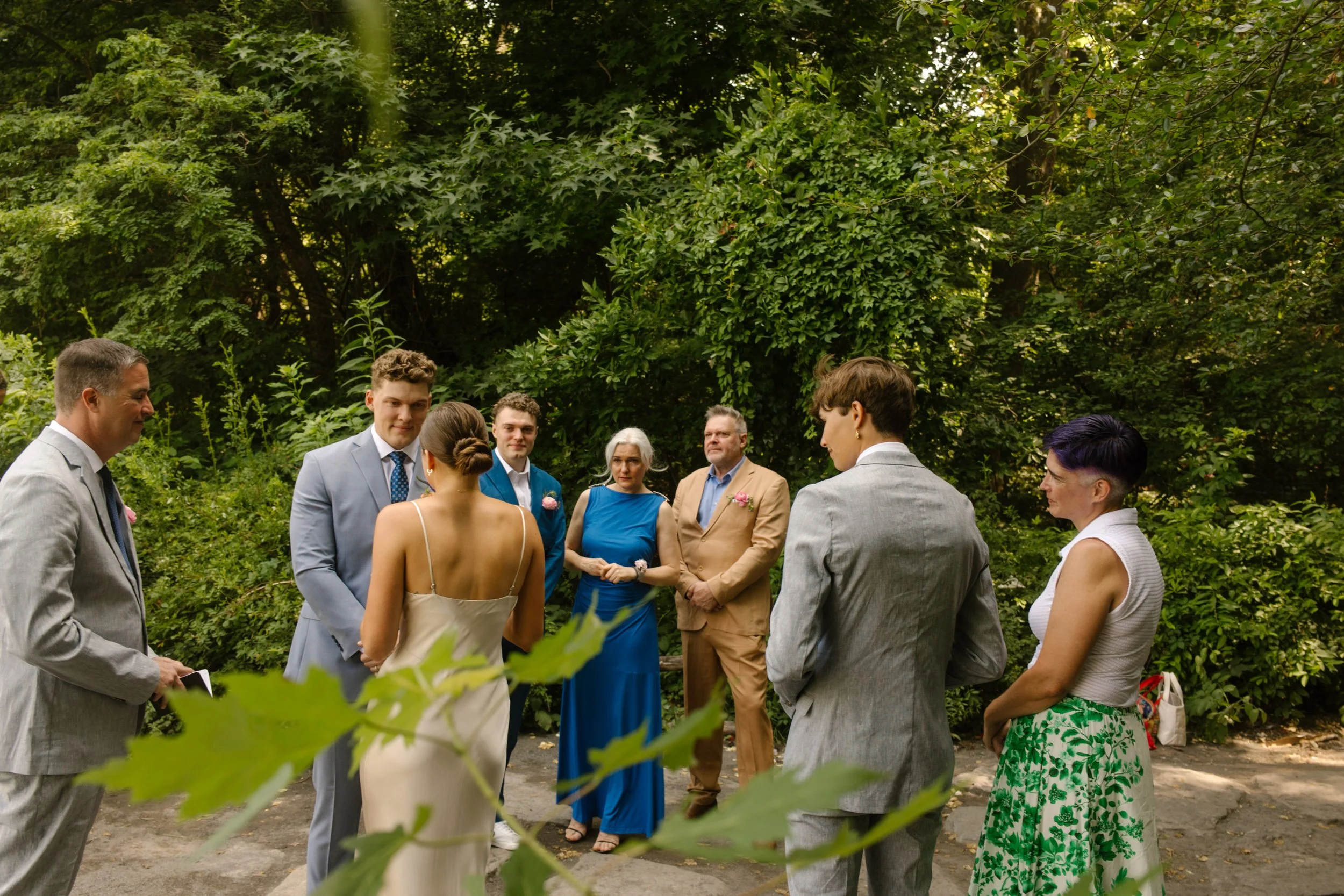 A small group gathers in a tucked-away clearing, watching as the couple begins their Central Park vows—an intimate New York City elopement surrounded by nature.