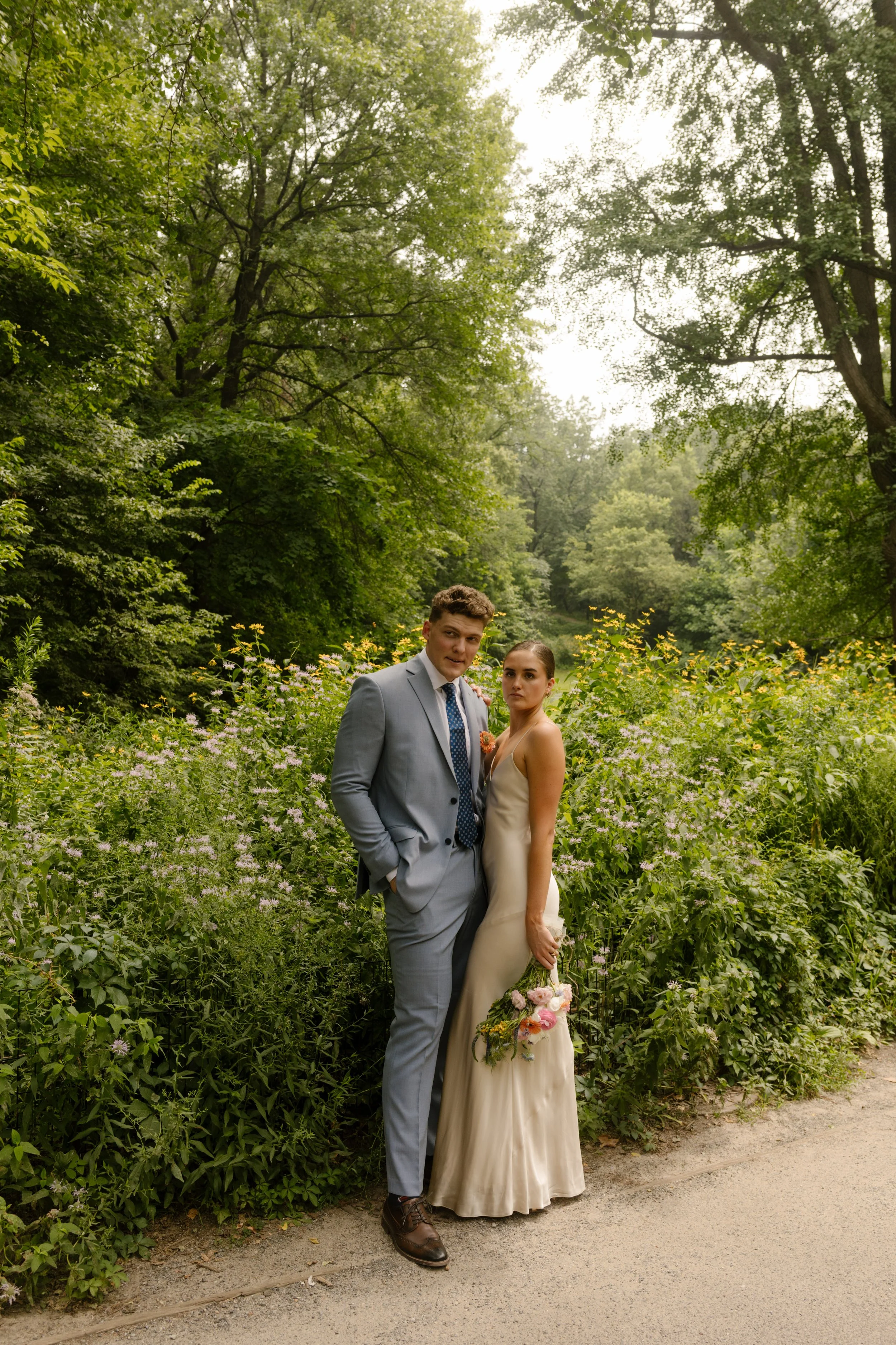 New York City elopement couple standing close, bouquet in hand, surrounded by untamed wildflowers and soft summer light.