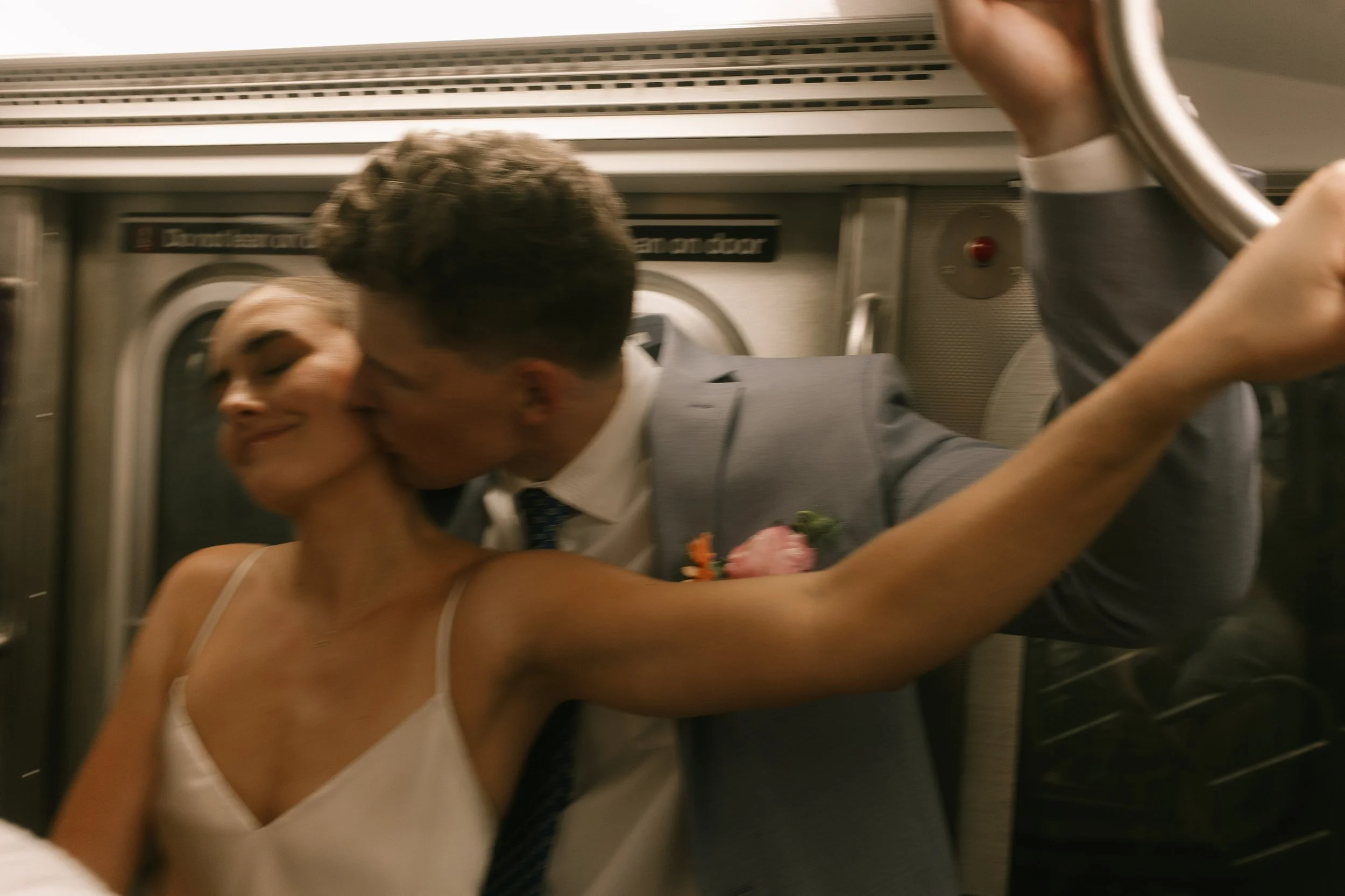 Playful moment on the subway with the groom kissing the bride’s cheek as she smiles.