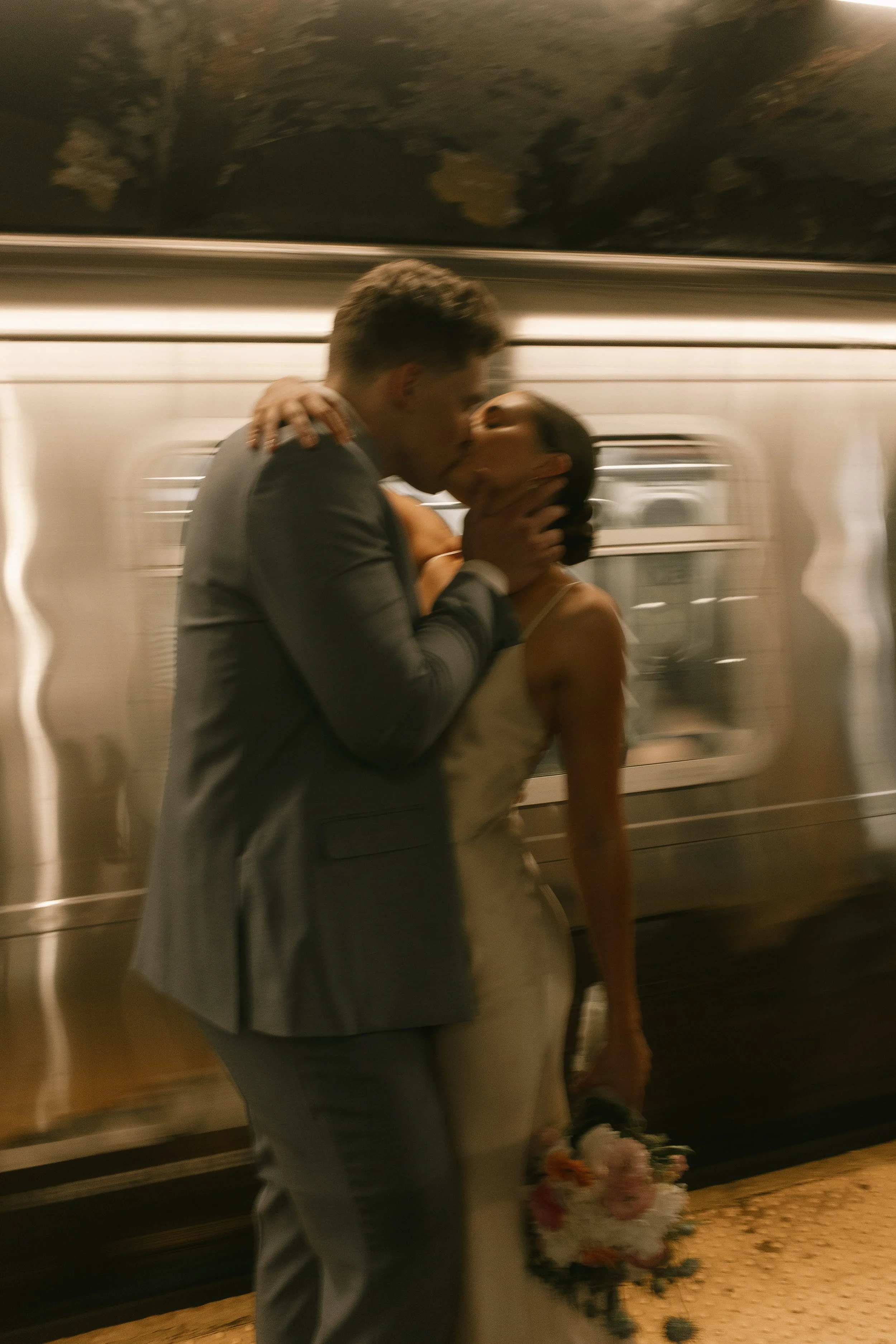 Dramatic kiss in front of a moving subway train, bouquet in hand.