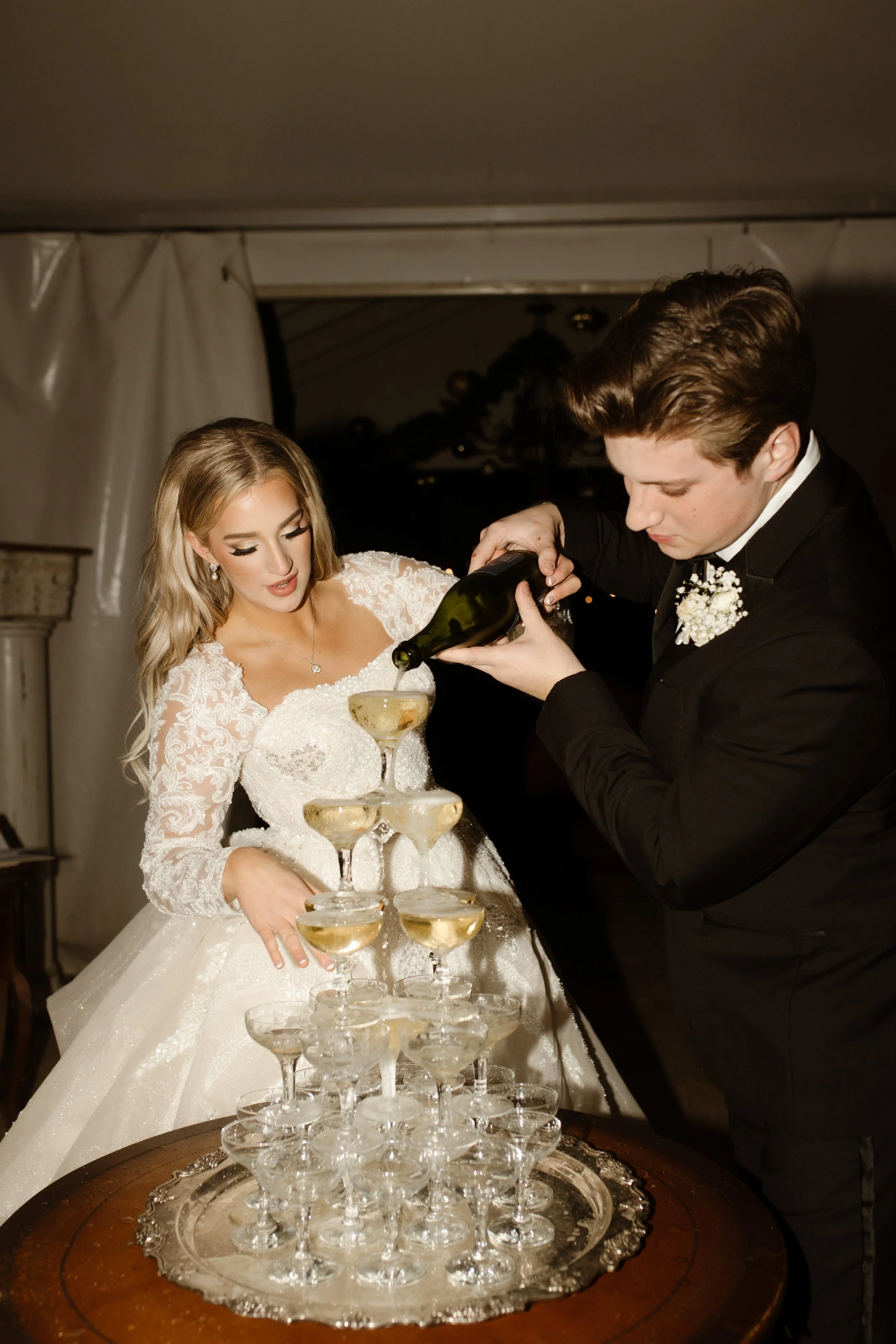 The couple pours champagne into a vintage coupe tower, laughter bubbling over just like the drinks at their Arkansas wedding reception.