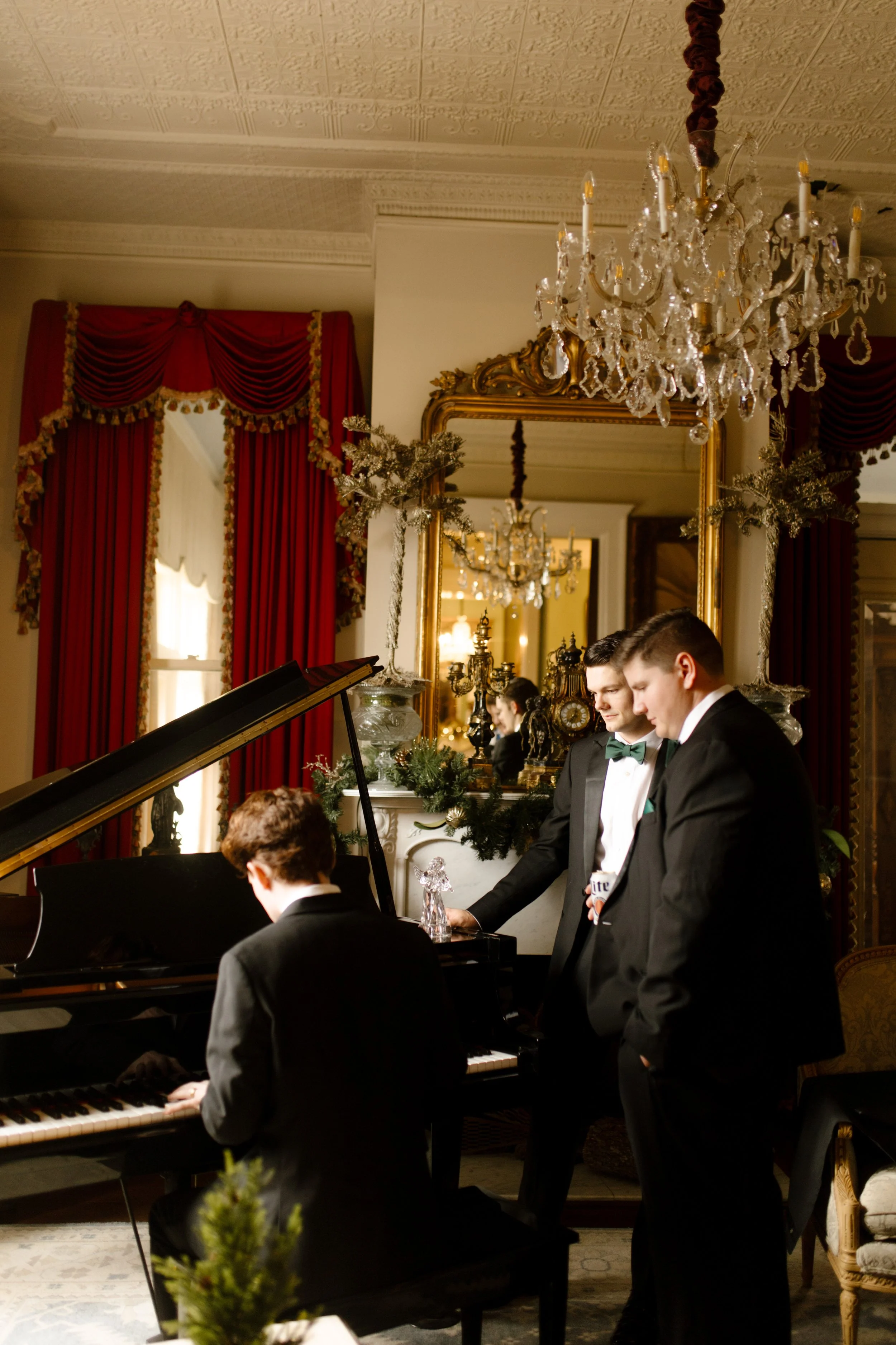 Groomsmen gather around a grand piano, sharing a quiet, golden-lit moment before the celebration begins.