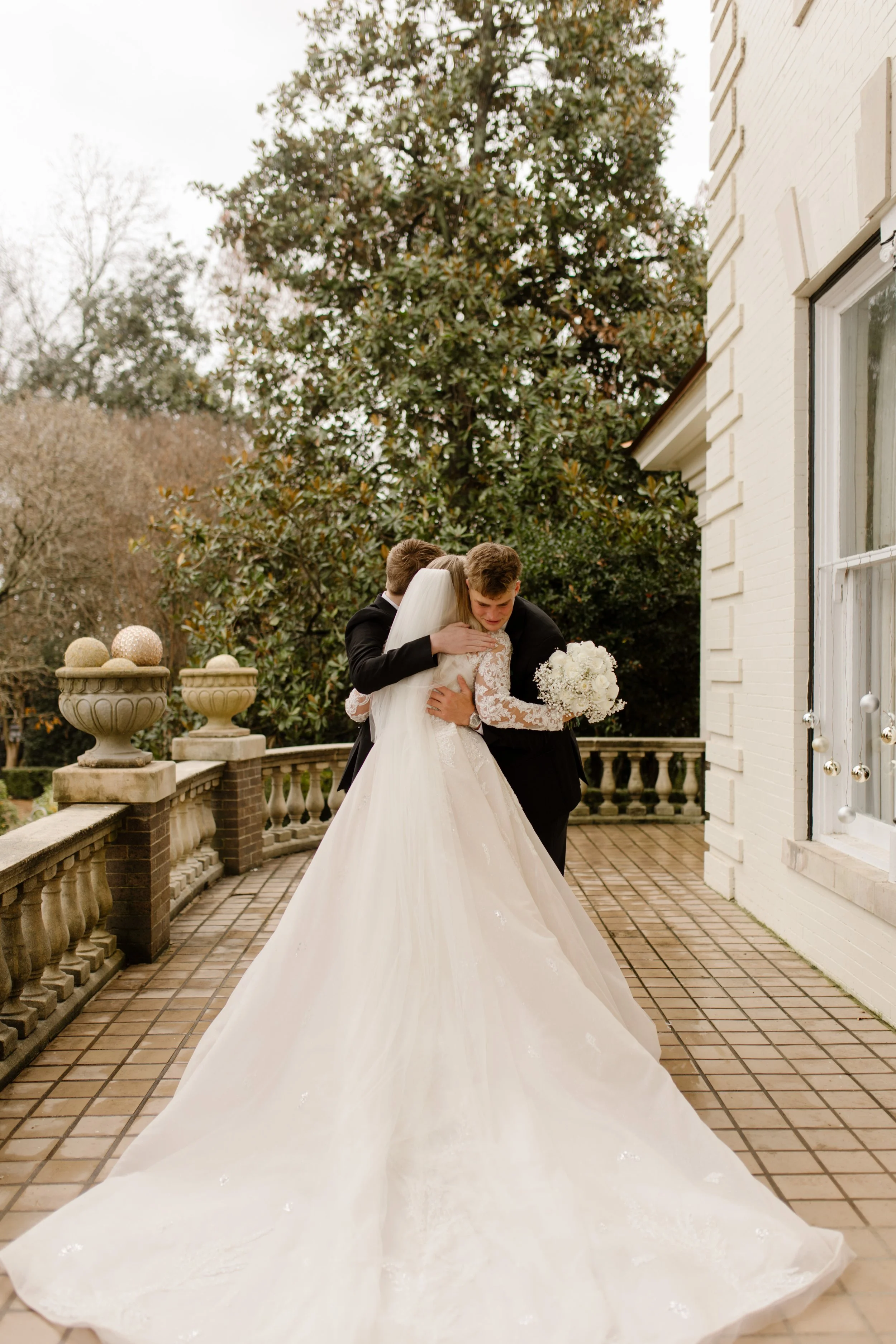 Bride embraces a loved one in a long, emotional hug on the terrace, her train pooled behind her in a quiet Arkansas wedding moment.