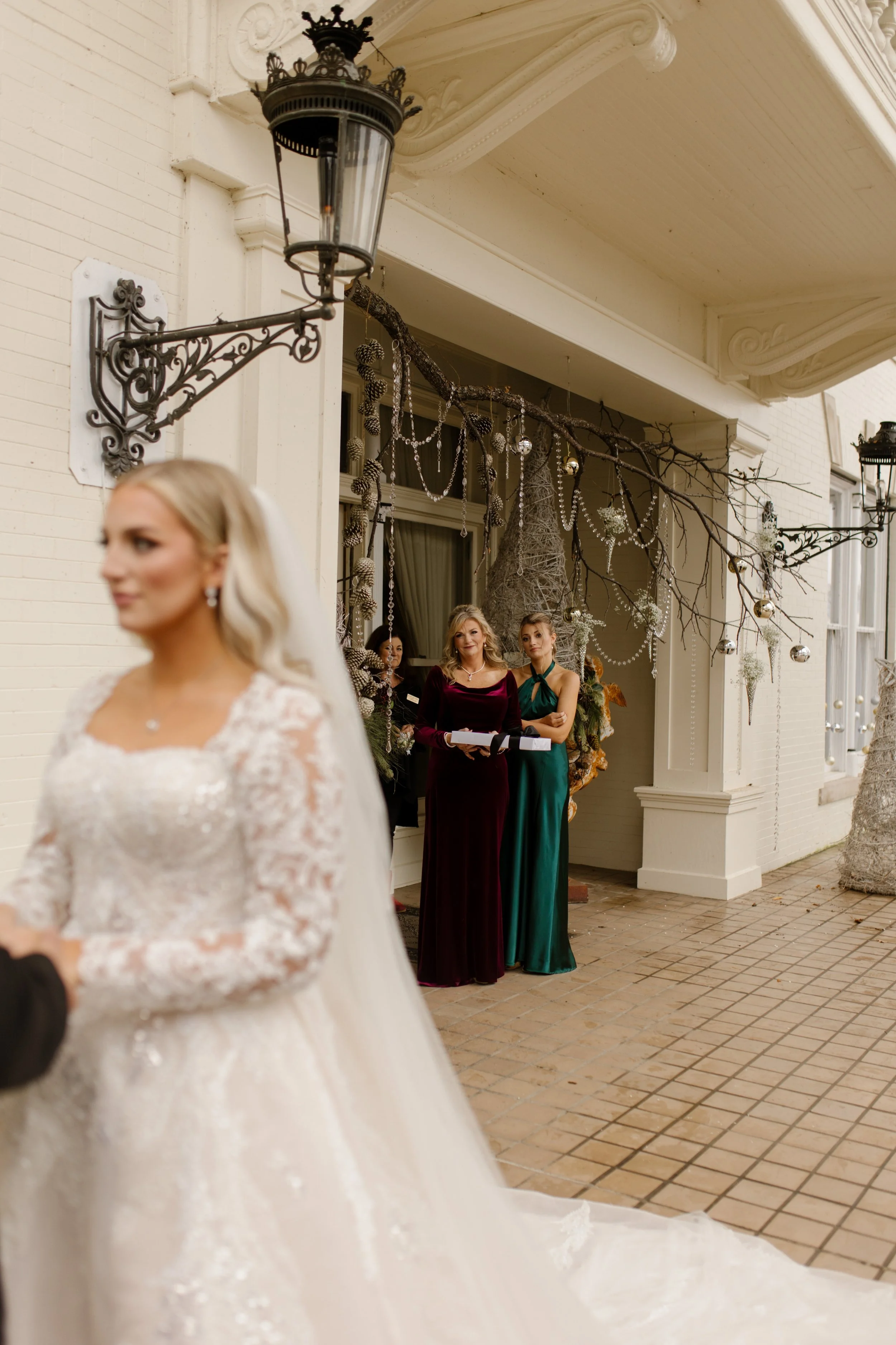 The bride shares a pre-ceremony moment while her mom and bridesmaids watch from the doorway, emotions already bubbling up.
