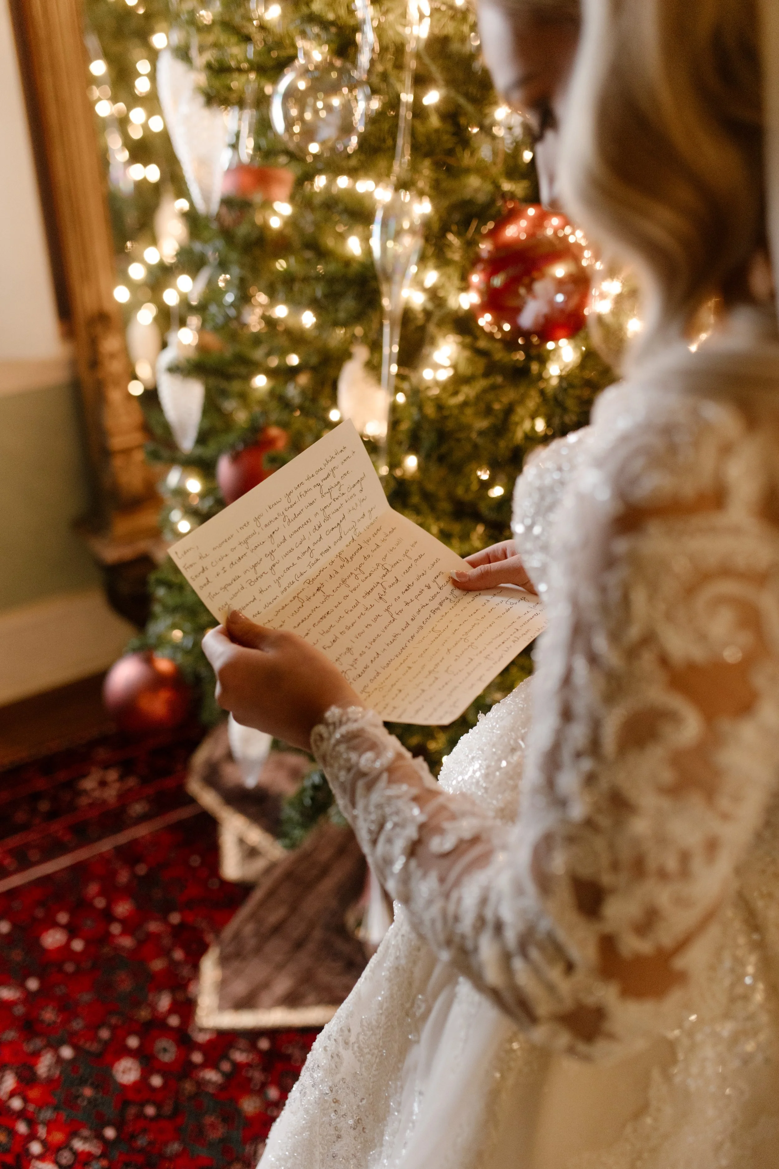 The bride reads a handwritten note beside a glowing tree, wrapped in lace and love at her winter Arkansas wedding.