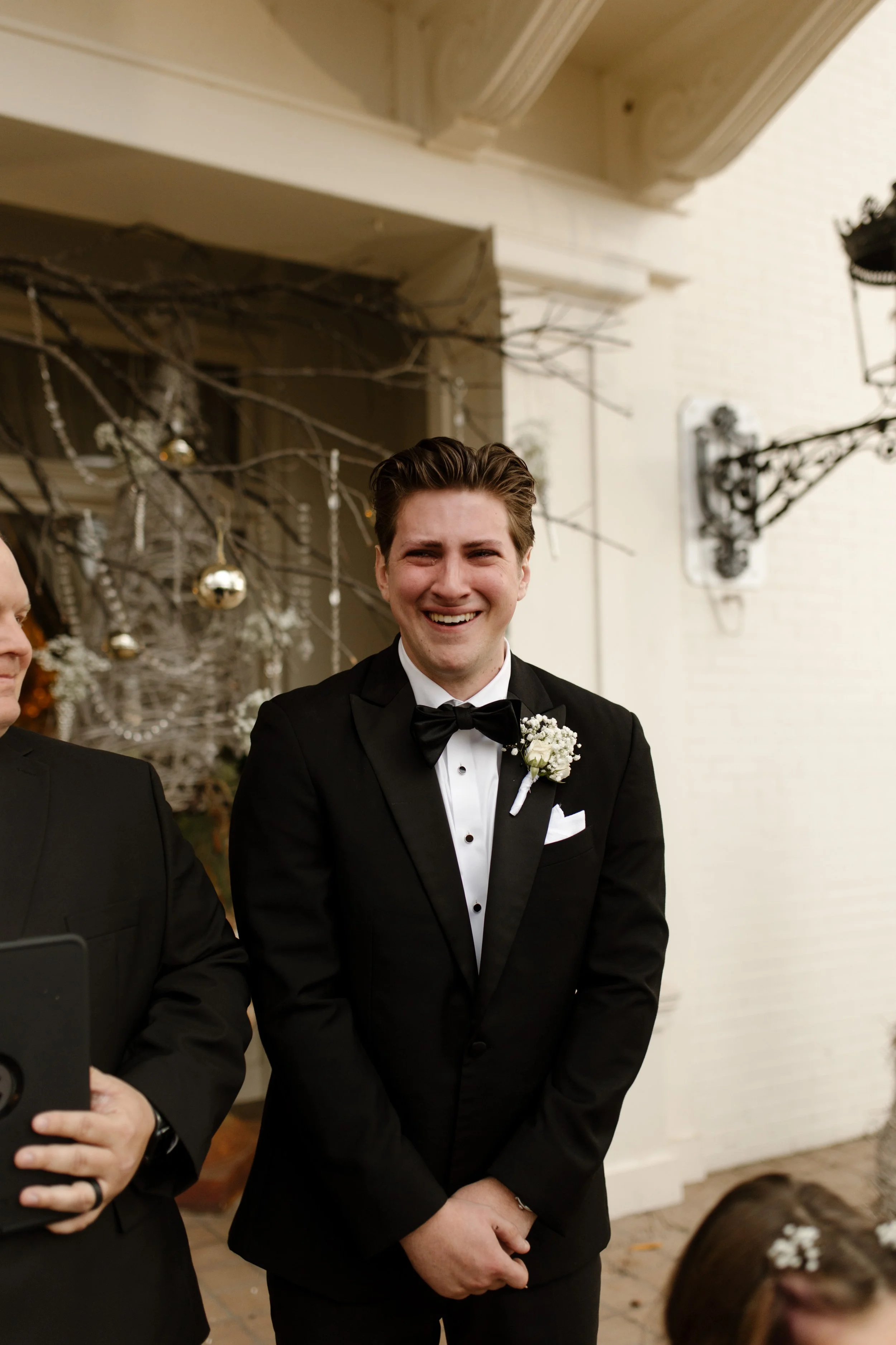 Groom grins with anticipation as he stands at the altar, dressed in classic black tie, waiting to see his bride at their Arkansas wedding.