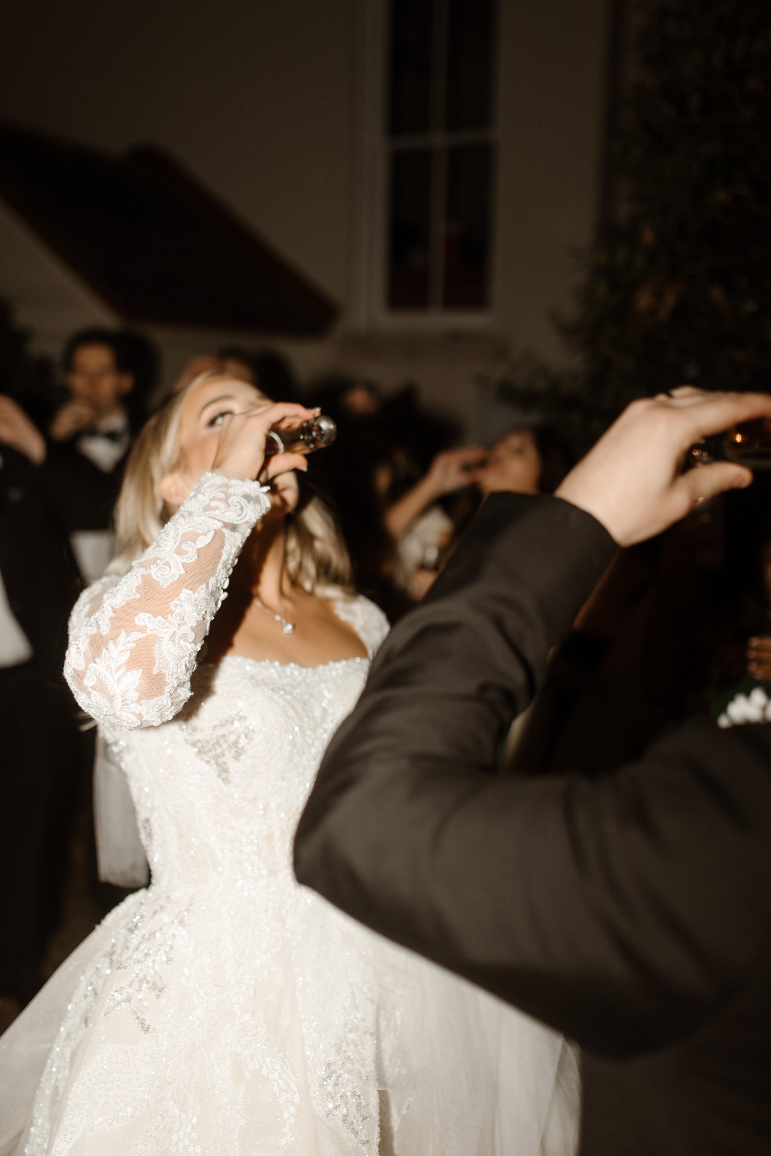 Bride throws back a celebratory shot in her wedding dress, surrounded by guests in a joyful moment of party-mode energy at their Arkansas wedding.