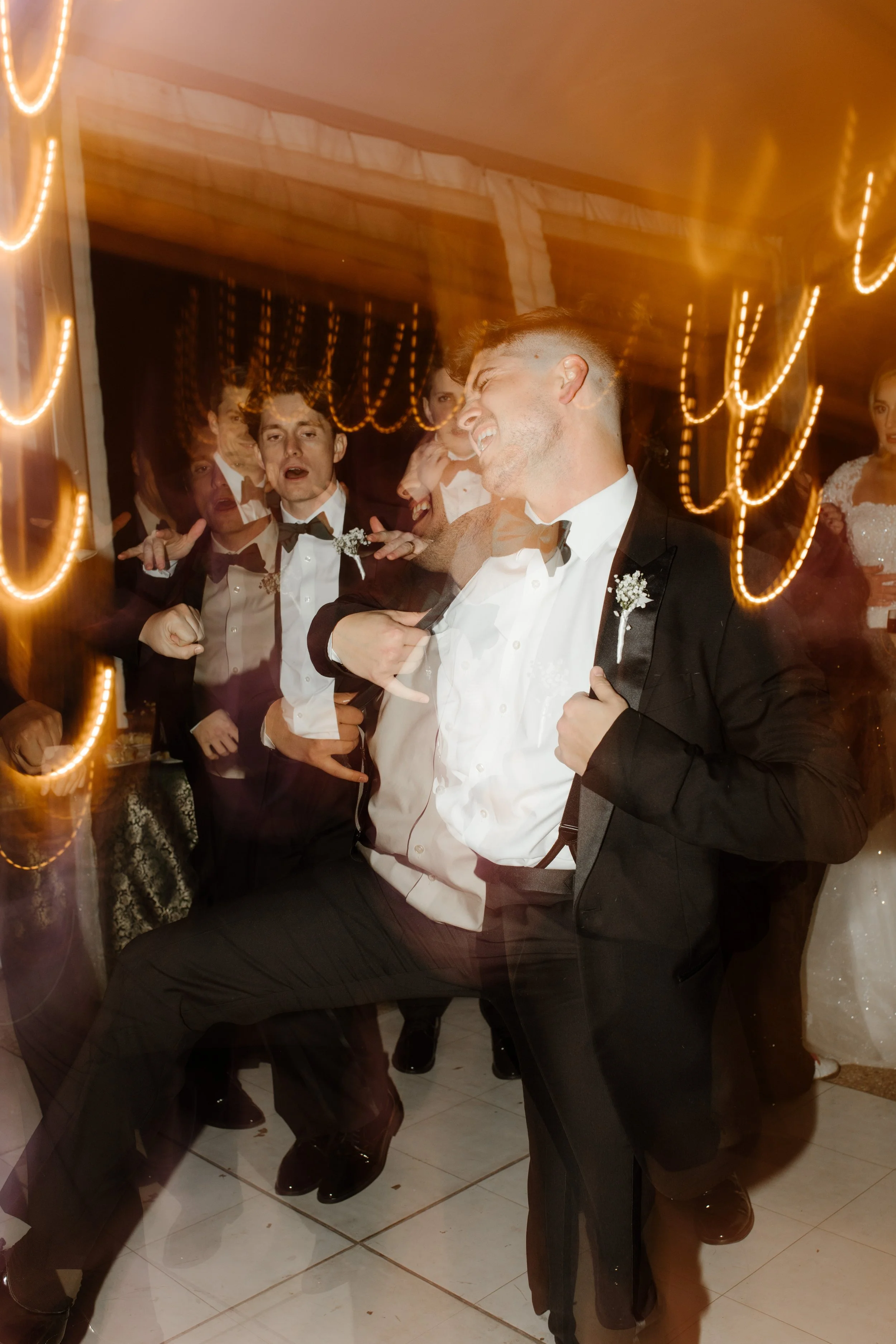 A flower girl in a tulle dress is lovingly embraced at the reception, with adults gathered around, soaking in the family-filled sweetness of the night.