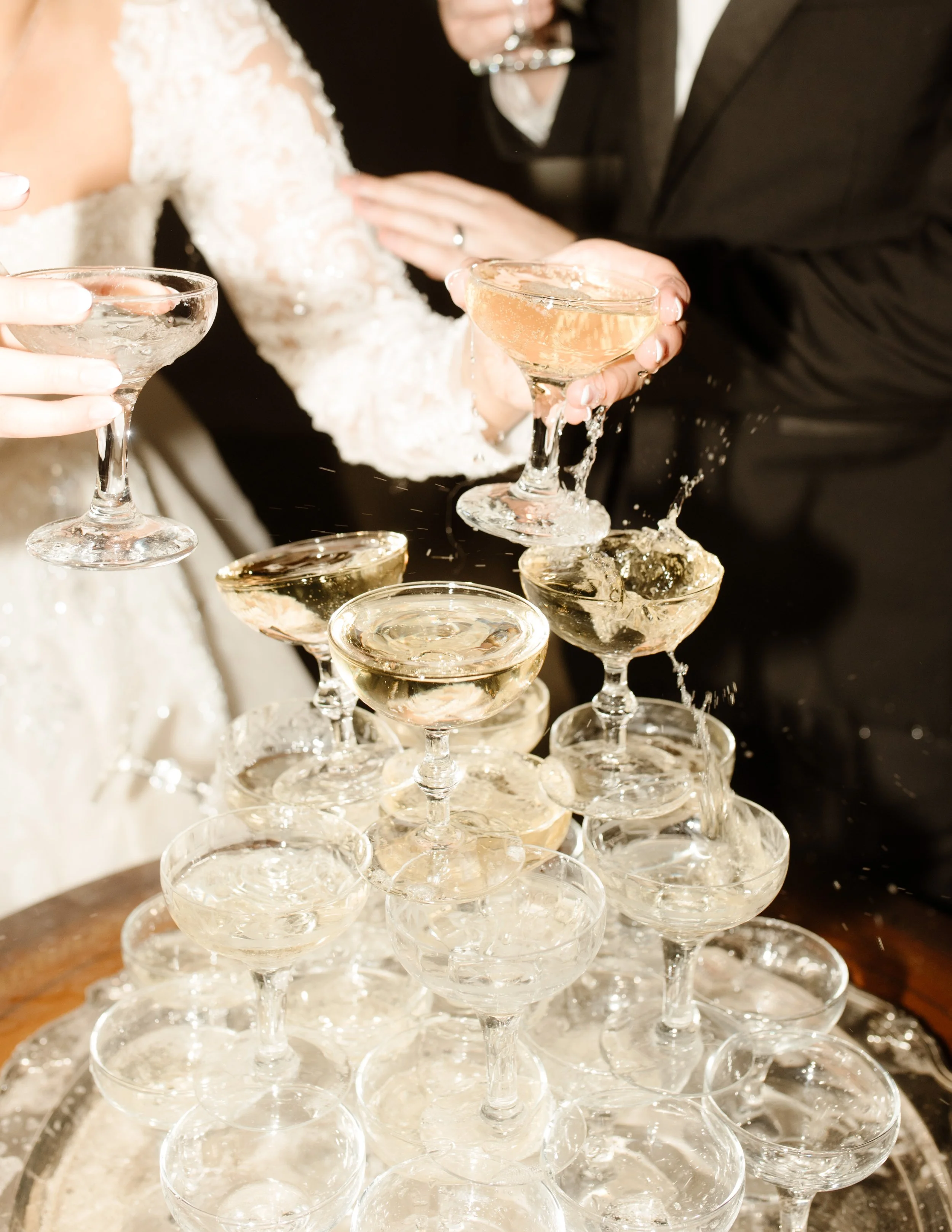Champagne splashes as the couple clinks glasses over a cascading tower—one of those “just married” moments that screams celebration.