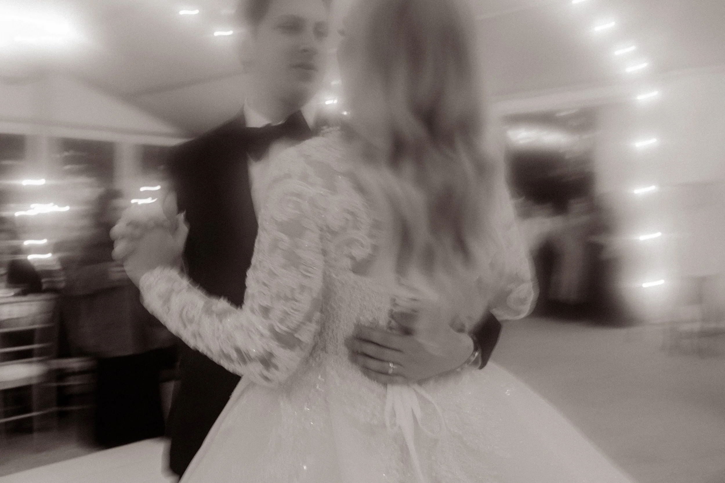 Blurry and beautiful—bride and groom share their first dance under glowing lights, a dreamy, slow-motion kind of love.