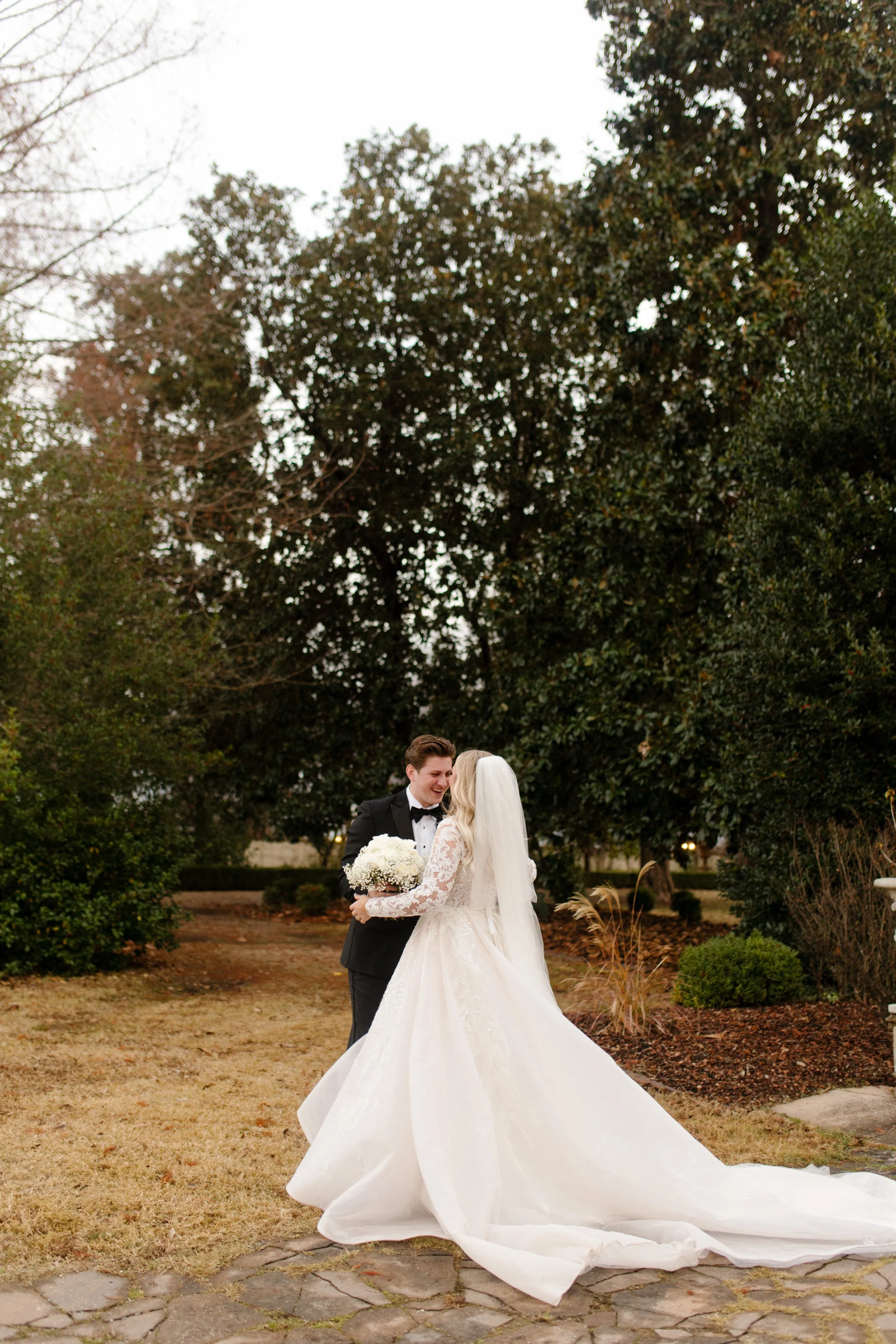 The couple holds each other close in a quiet moment outside, her cathedral-length veil trailing behind them during their intimate Arkansas wedding.