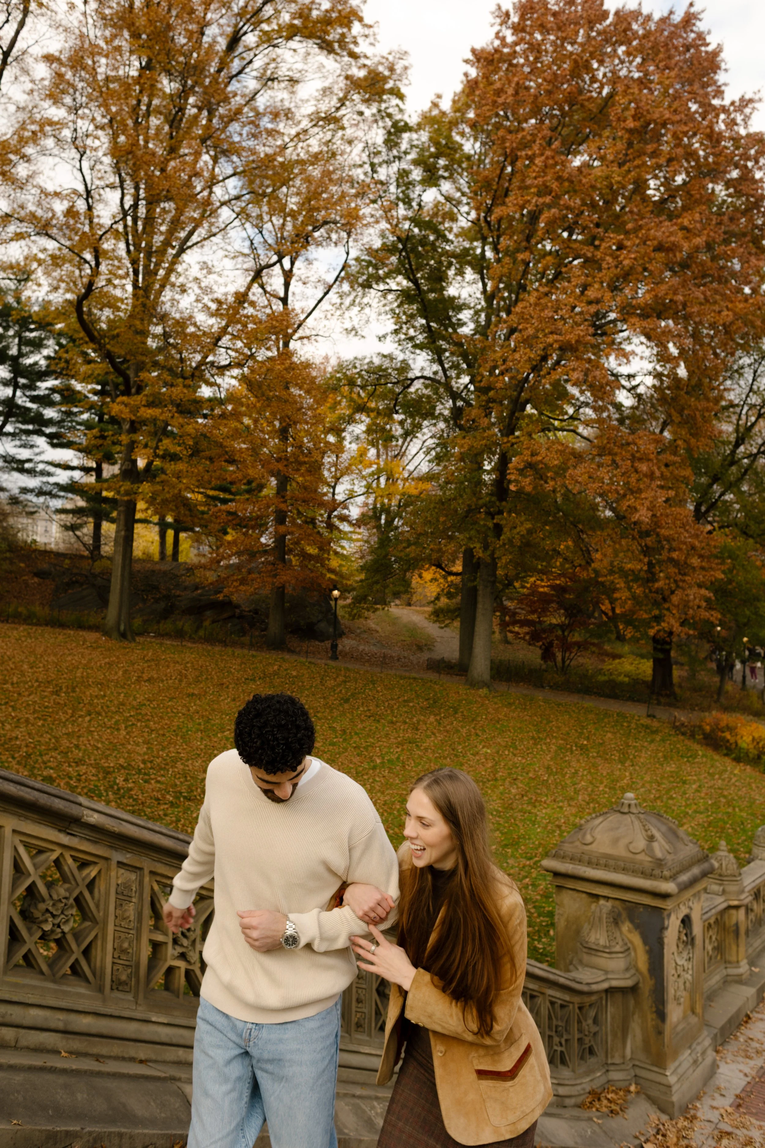 Couple laughing and holding hands while walking up the stone steps during a Central Park photoshoot.