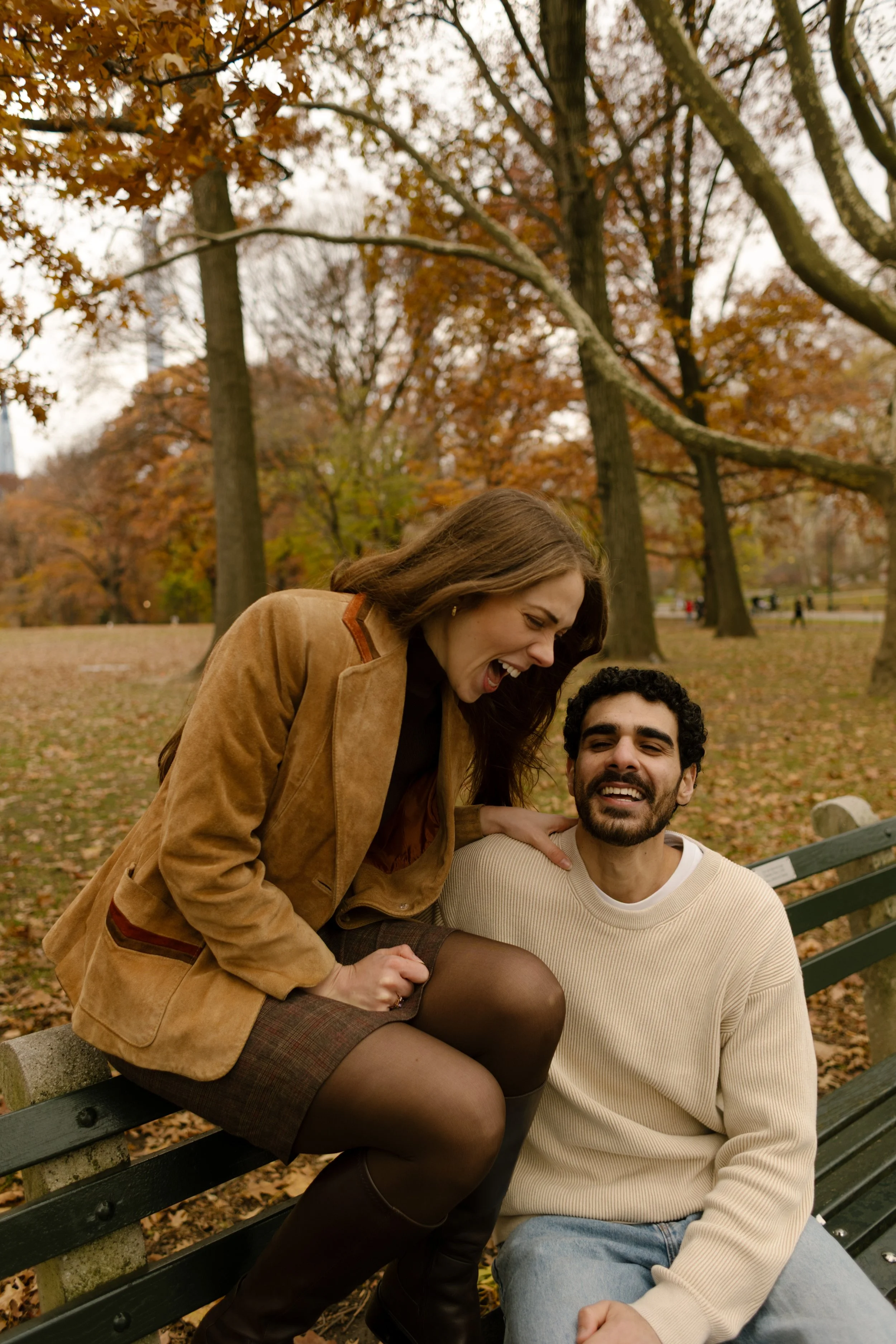 Couple laughing out loud on a bench in Central Park, surrounded by orange and rust-colored leaves.