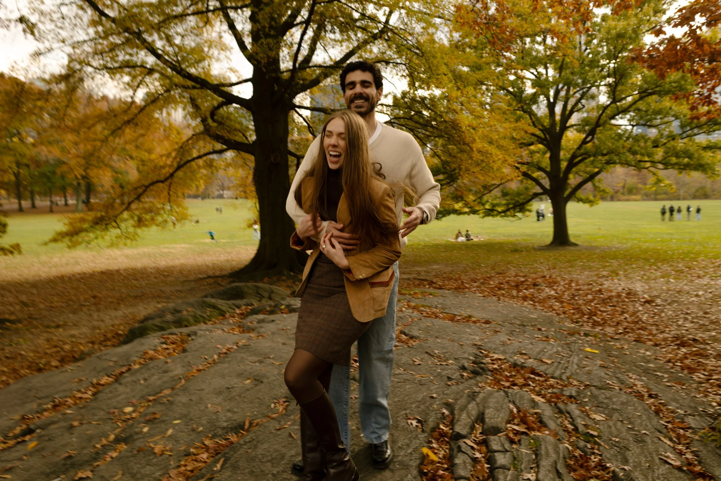 Couple laughing as they spin and play on a rock in Central Park, wrapped in warm fall colors.