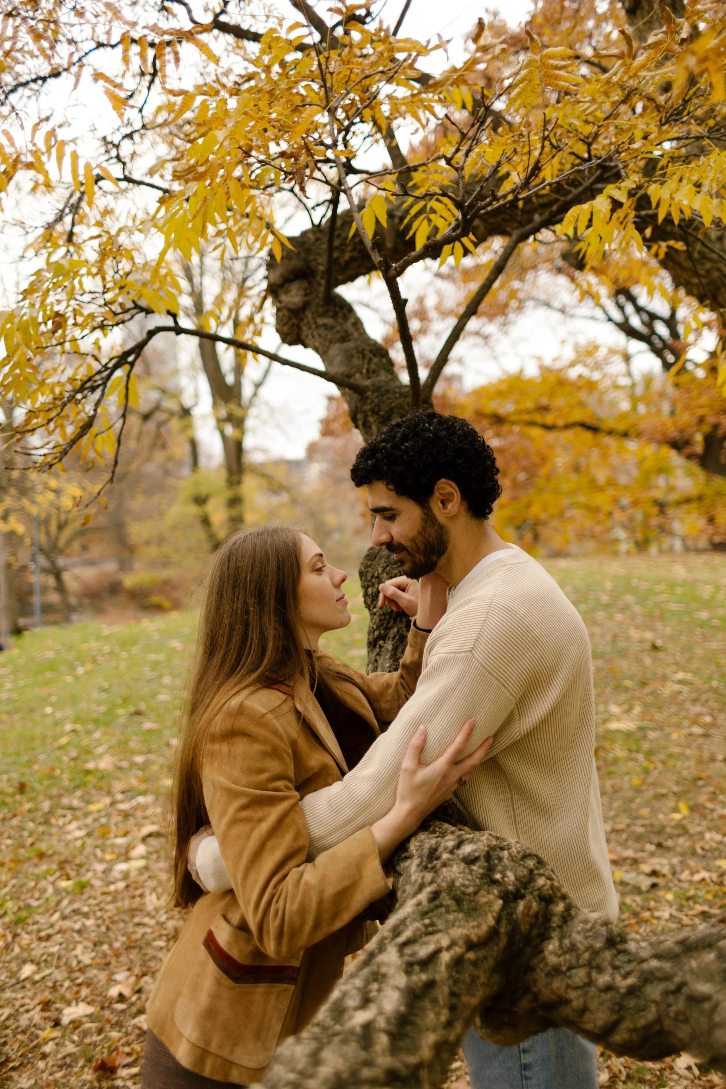Cozy eye contact and gentle touch between a couple framed by low-hanging branches during their Central Park photoshoot.