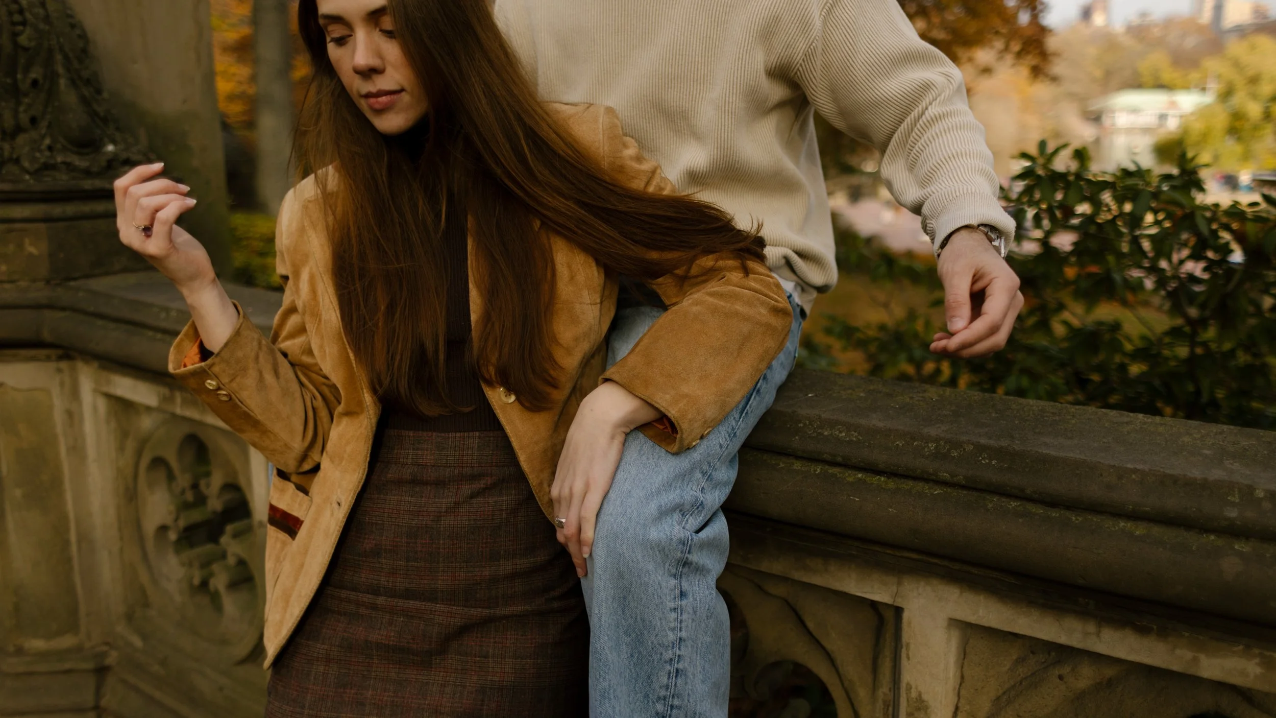 Cropped, candid detail of a couple leaning against a stone railing near Bethesda Terrace, showing hands and subtle connection.
