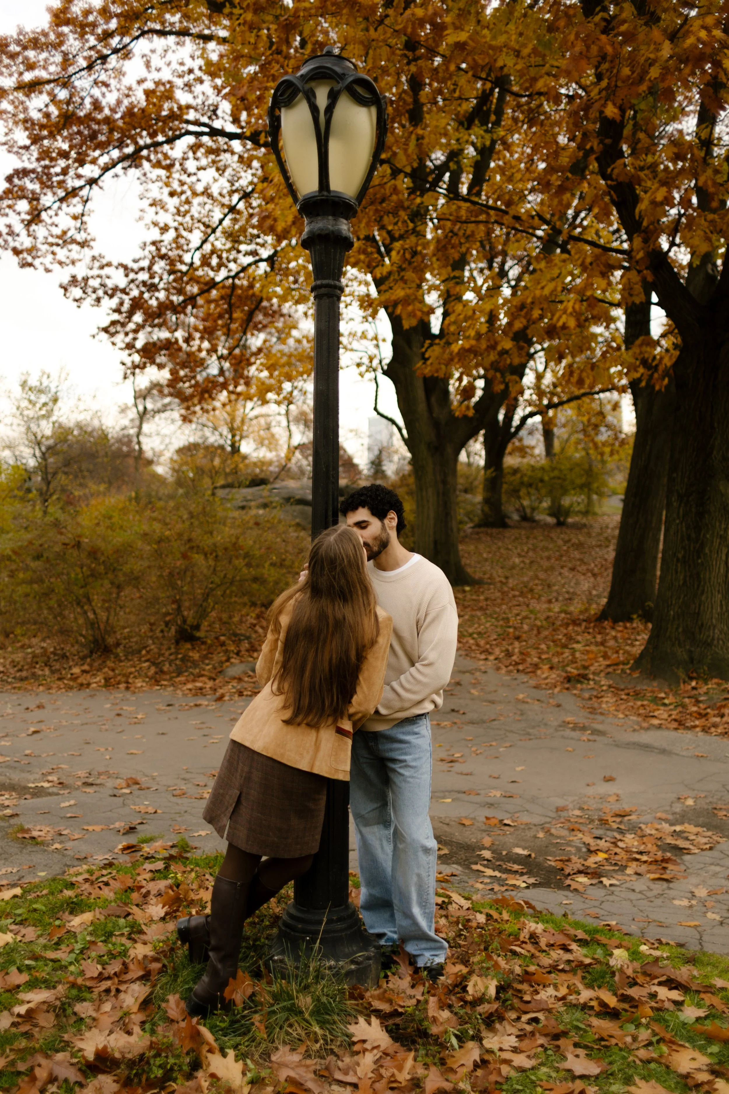 Intimate kiss under a vintage lamppost, wrapped in autumn trees during a quiet Central Park moment.