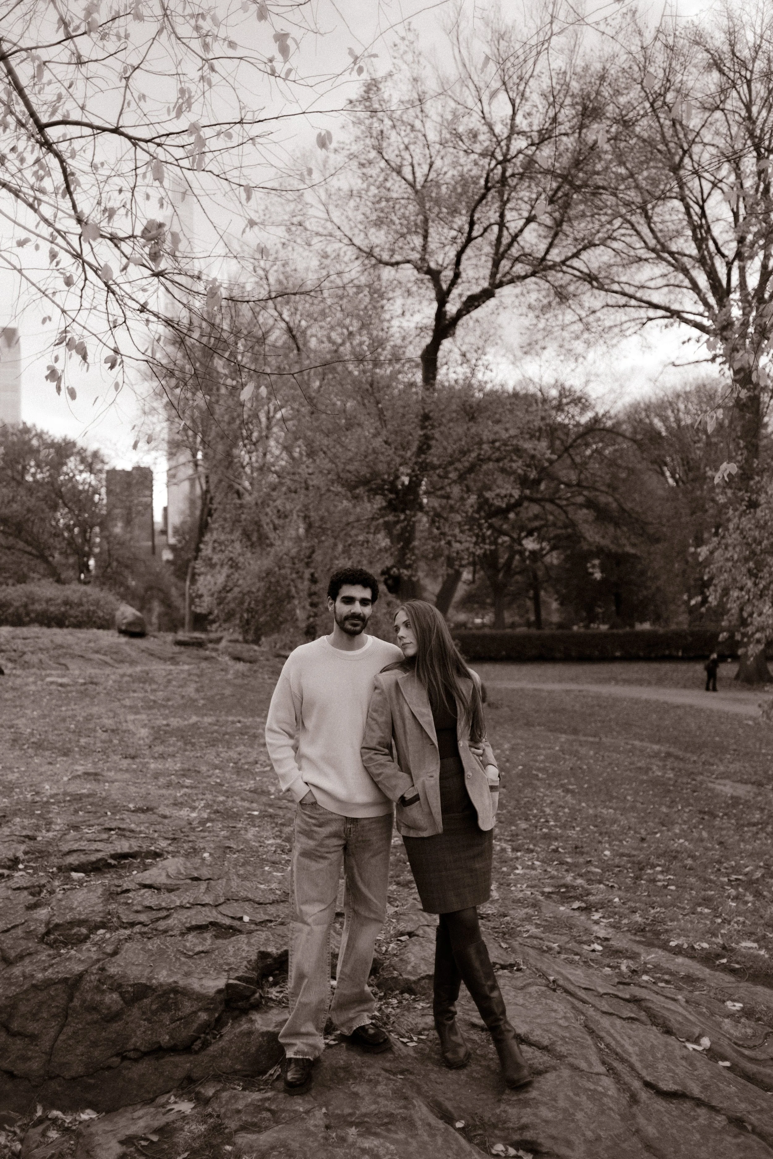 Black and white photo of a couple smiling and walking across the rocks in Central Park.
