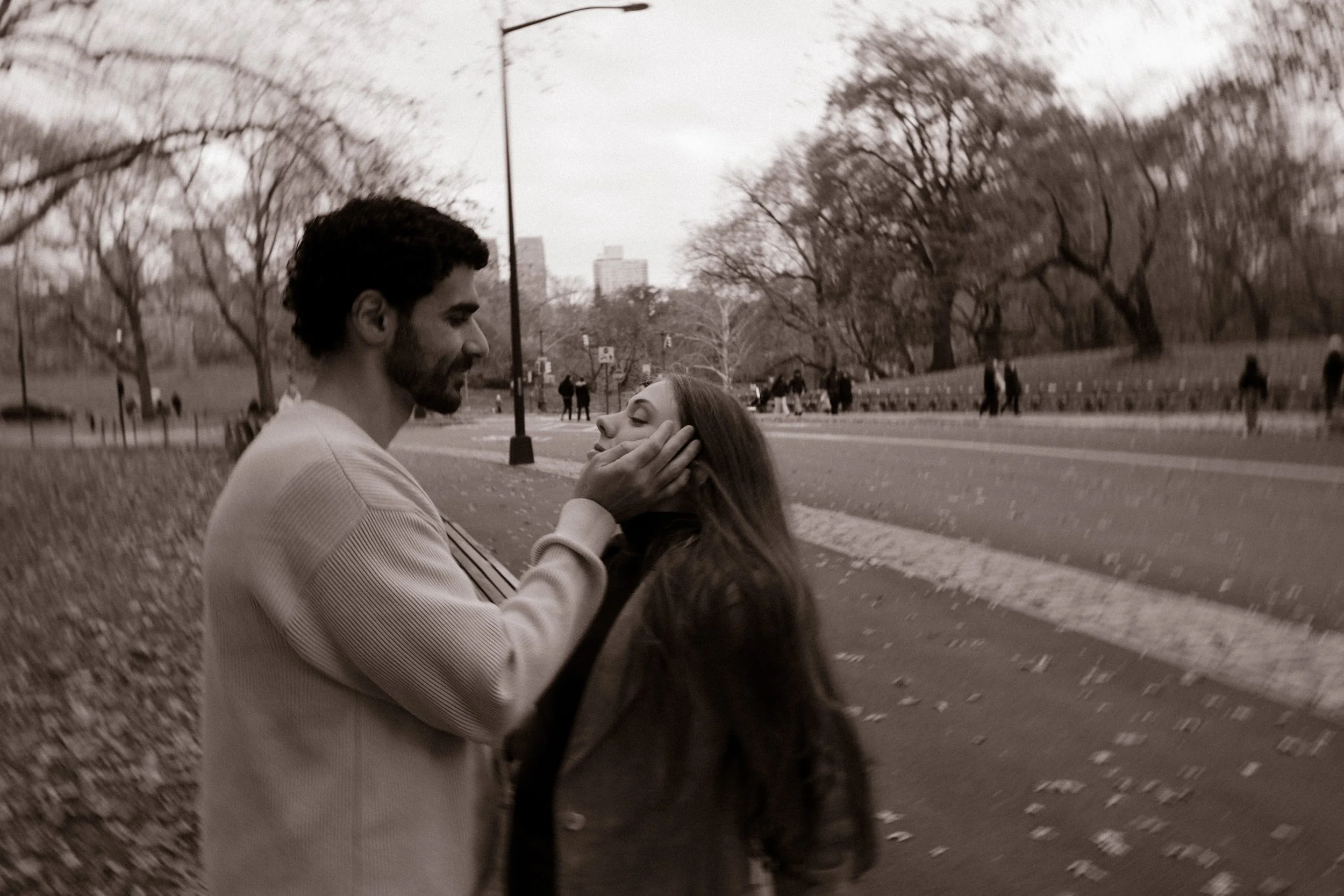 Black and white image of a couple smiling and holding each other’s faces on a Central Park walkway.