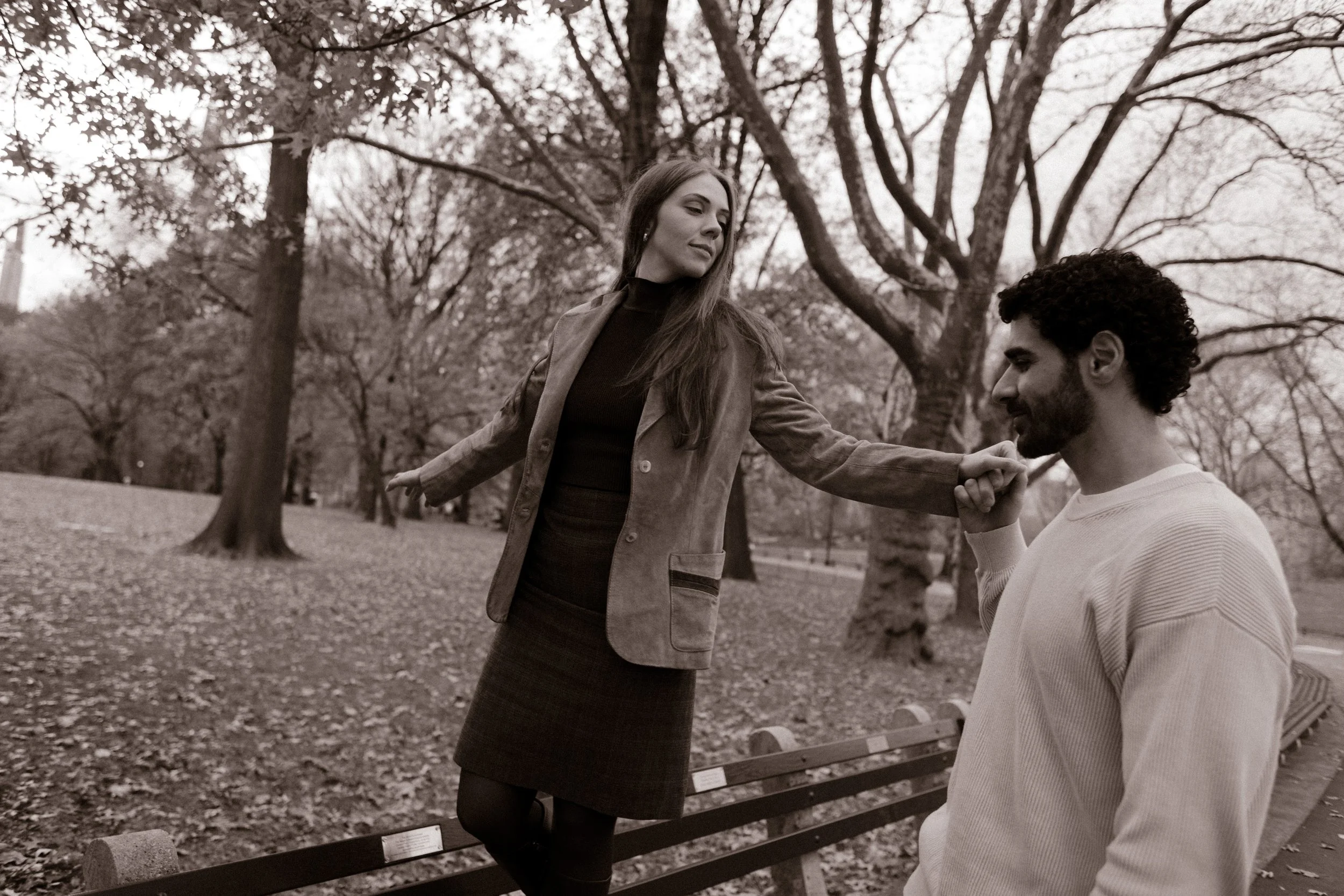 Vintage-toned photo of a woman balancing on a bench while her partner kisses her hand in Central Park.