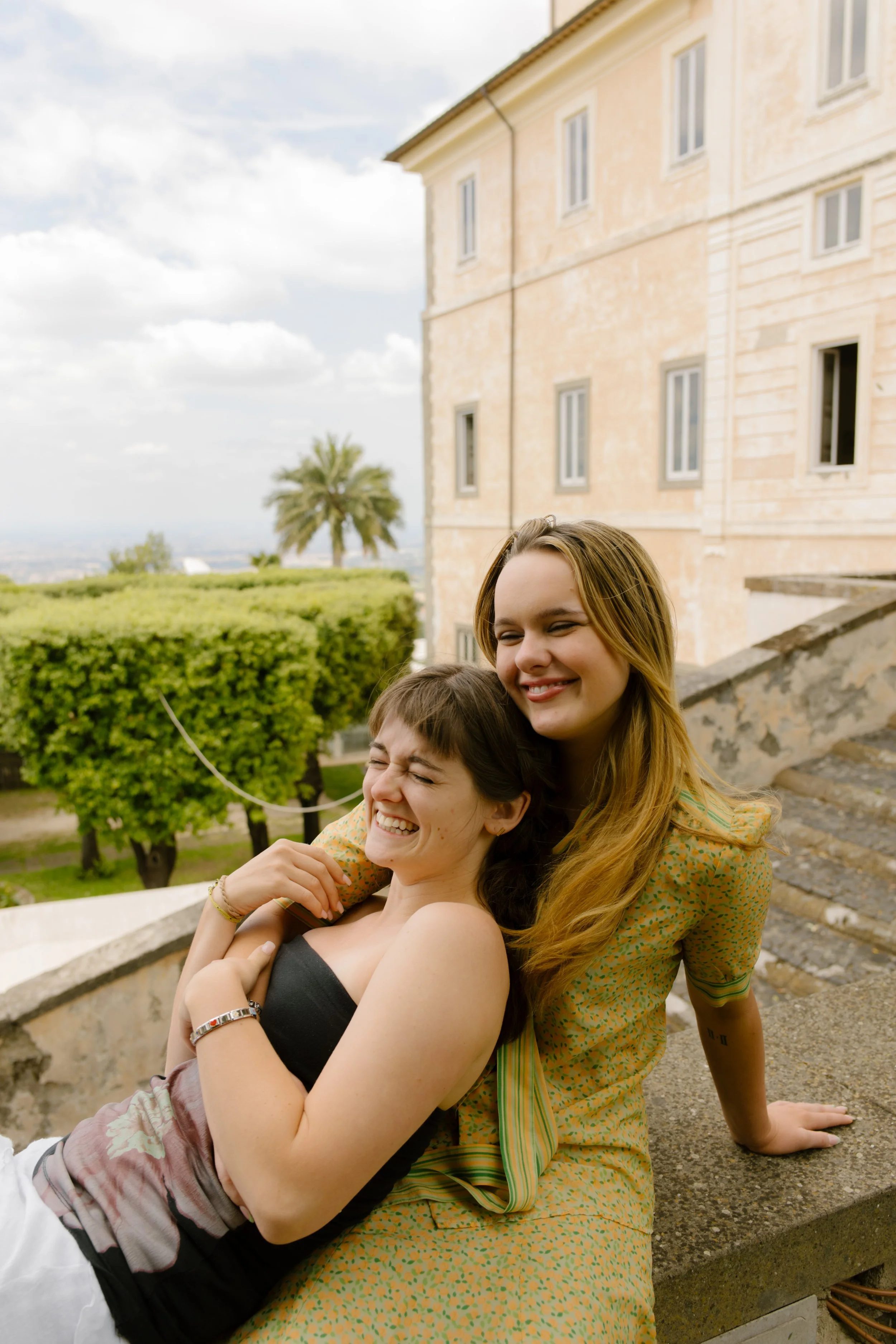 Two women sitting on roof hugging and smiling getting ready to celebrate upcoming wedding.