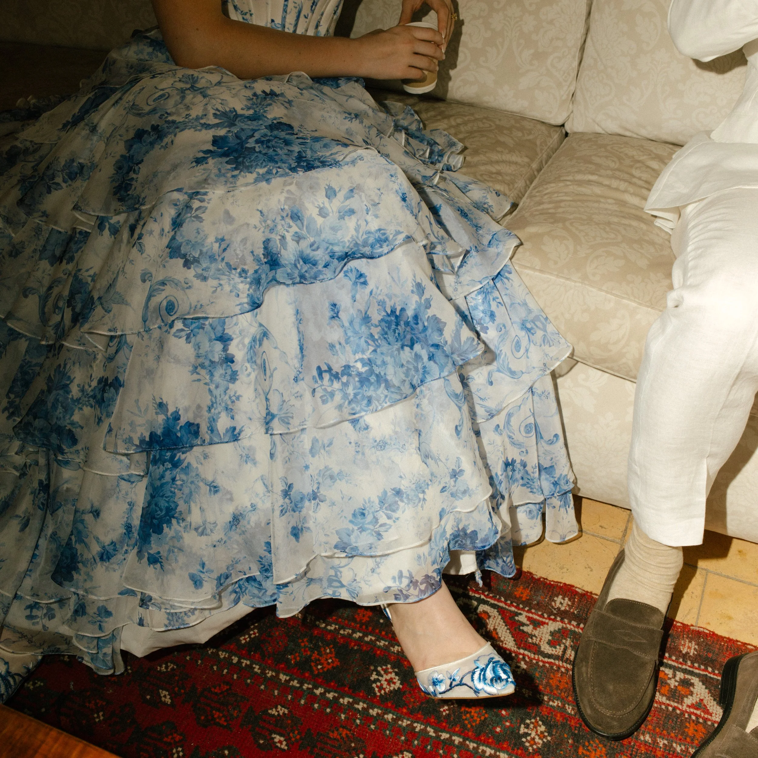 A close-up of the bride’s ruffled blue gown cascading across a vintage rug, delicate textures meeting soft light. Every layer tells a love story.