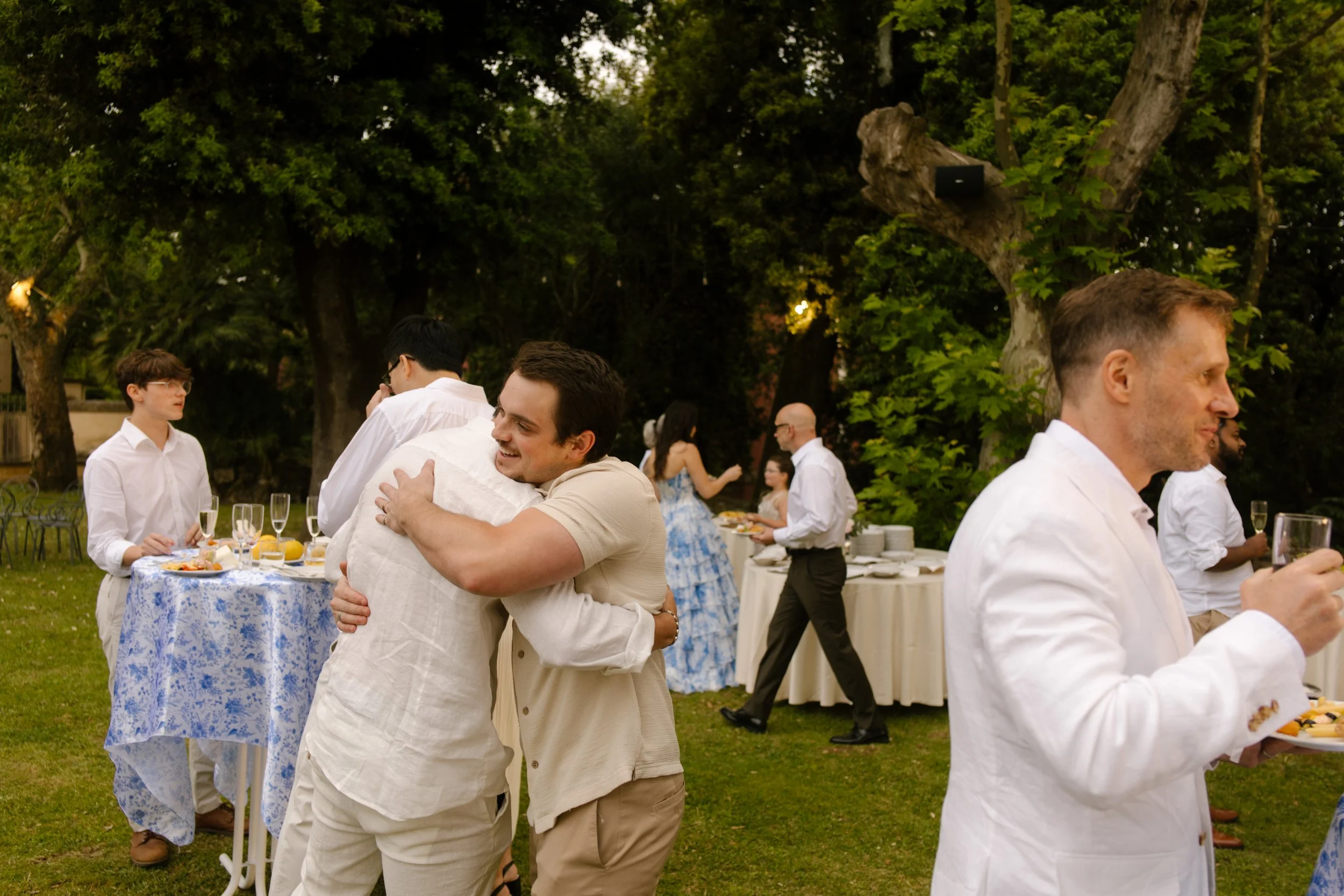 Friends embrace and laugh while mingling around cocktail tables and linen-clad buffets. A garden celebration full of hugs and heartfelt reunions.