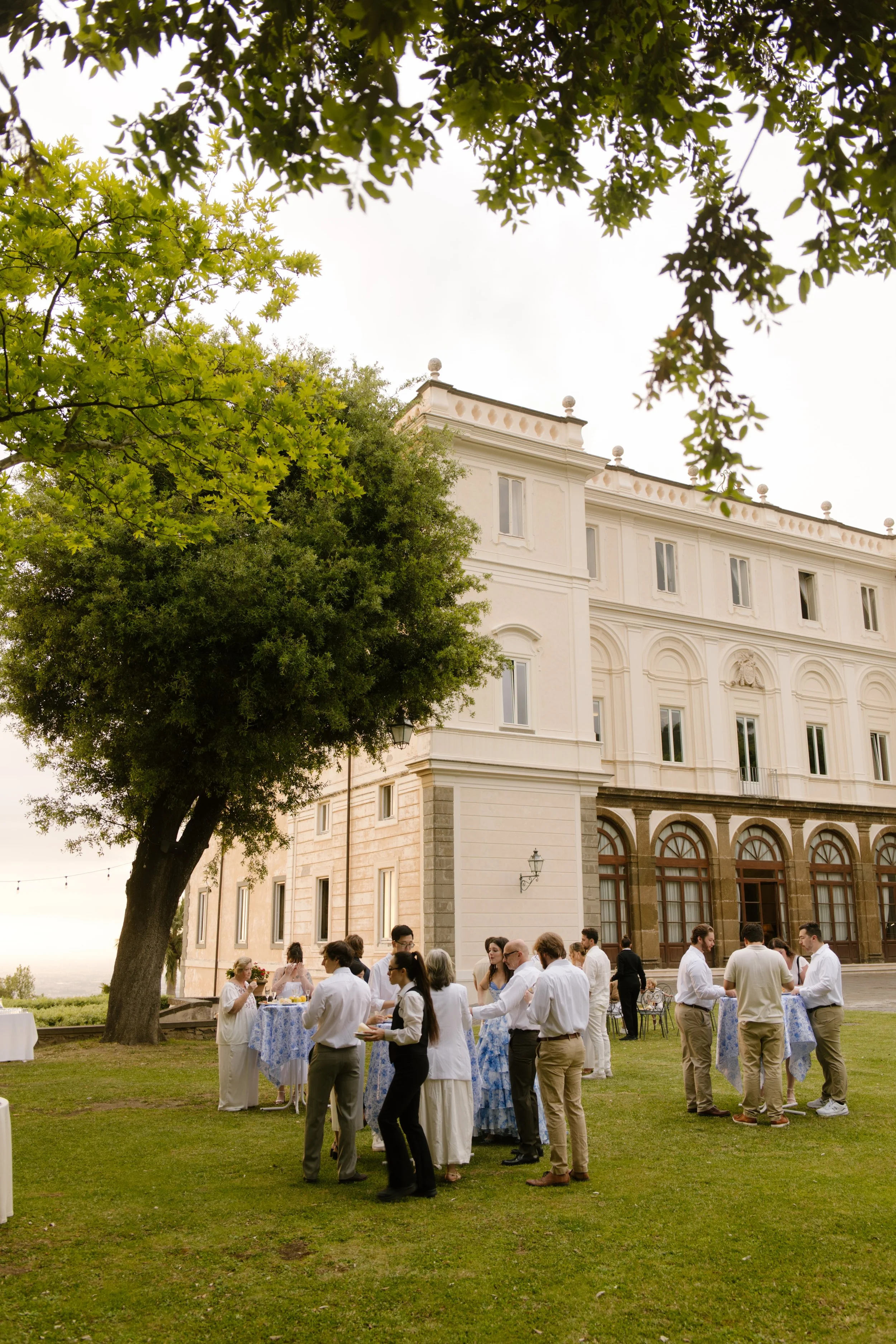 Groups gather in clusters on the villa lawn, drinks in hand and excitement buzzing in the air. Natural, candid moments captured during a wedding in Italy.