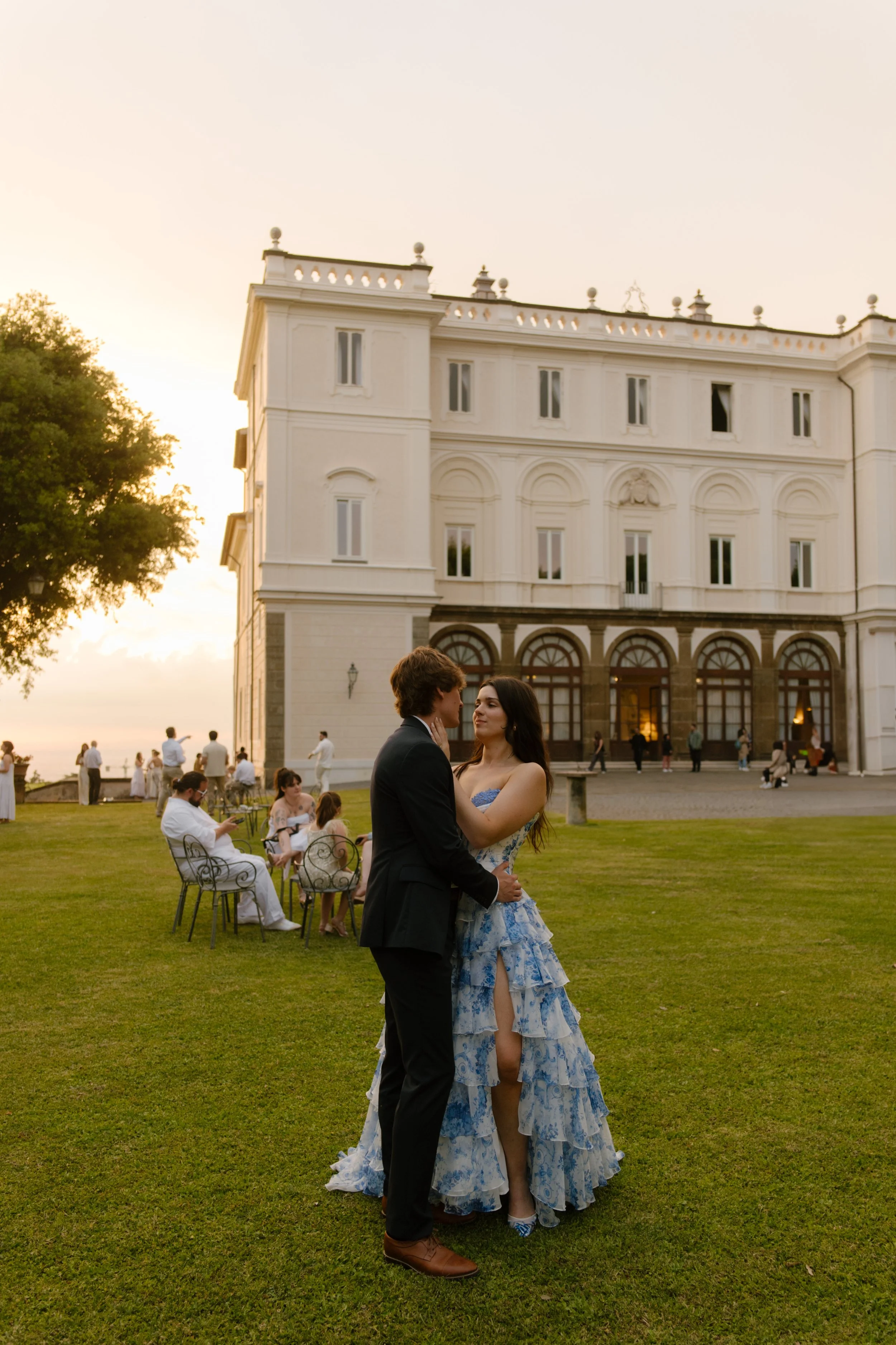 The couple shares a quiet first dance on the grass, villa glowing behind them as guests lounge nearby. A romantic dance moment during their wedding in Italy.