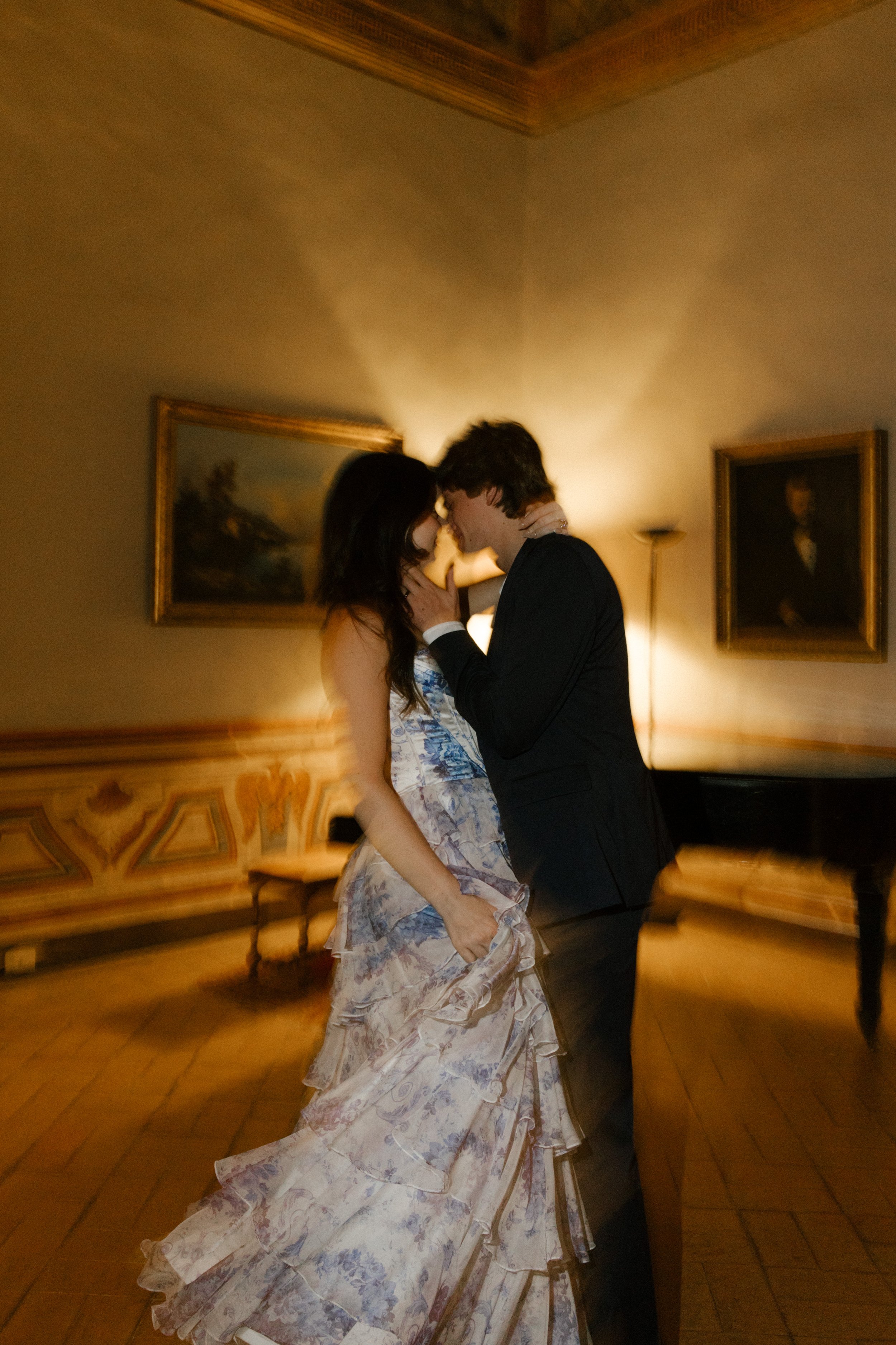 The couple shares a slow dance in a dimly lit villa room, surrounded by vintage paintings and love thick in the air. A romantic, candlelit moment after the party fades.