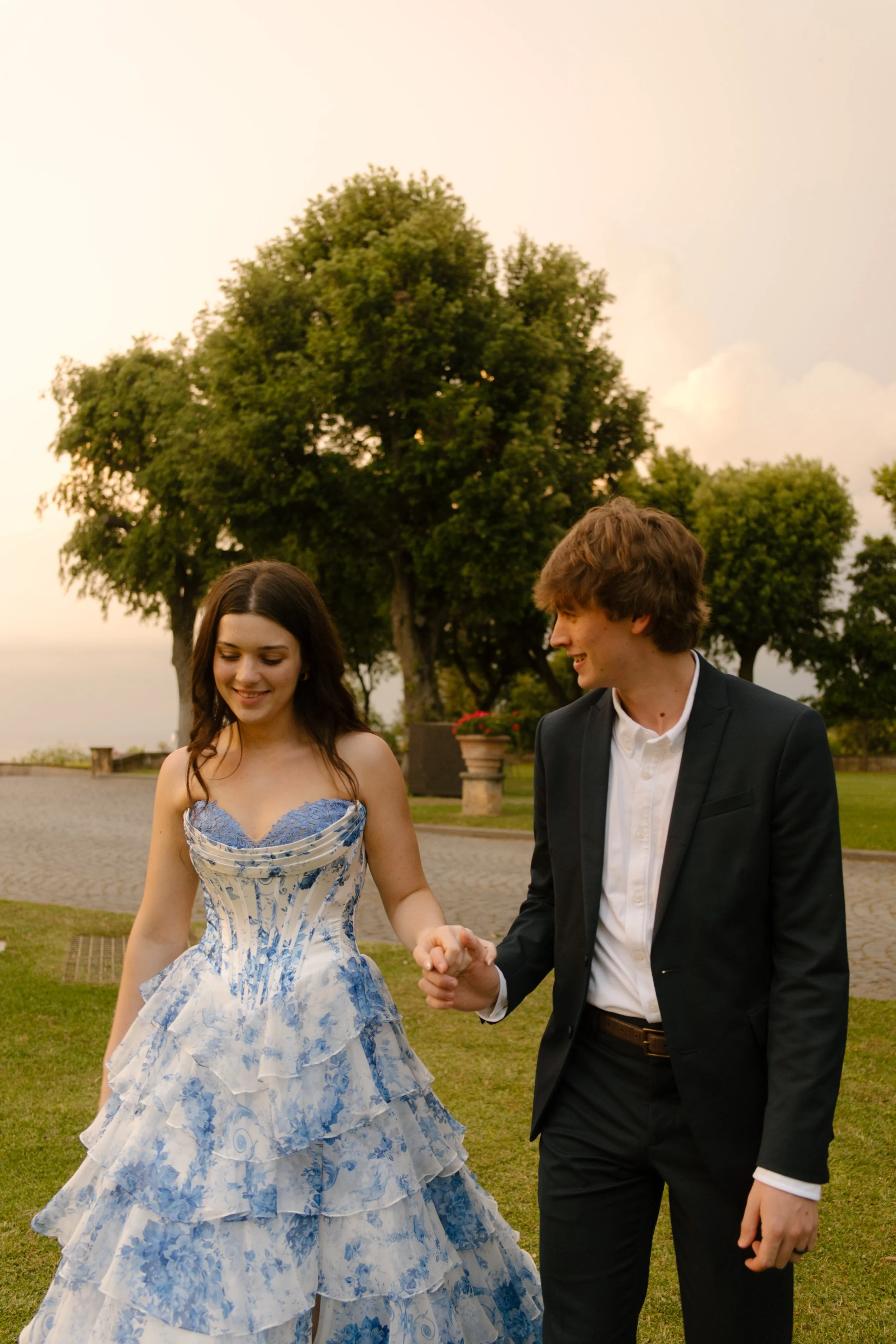 The couple holds hands and walks across the grass, caught mid-laugh as the sun dips low. Documentary-style magic during a wedding in Italy.