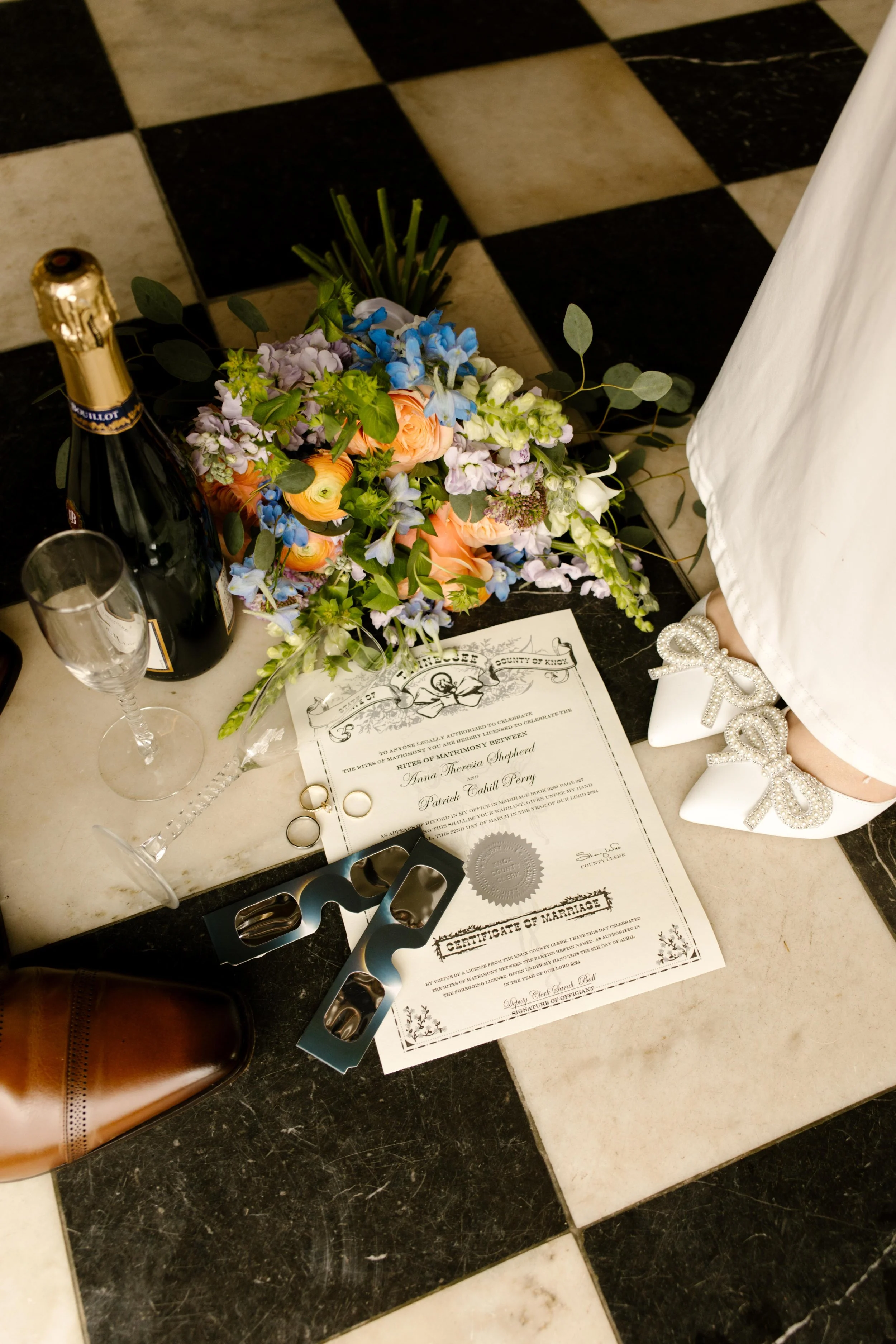 A champagne bottle, wedding rings, bouquet, certificate, and bride’s white shoes are artfully arranged on the courthouse floor—capturing Knoxville courthouse elopement details.