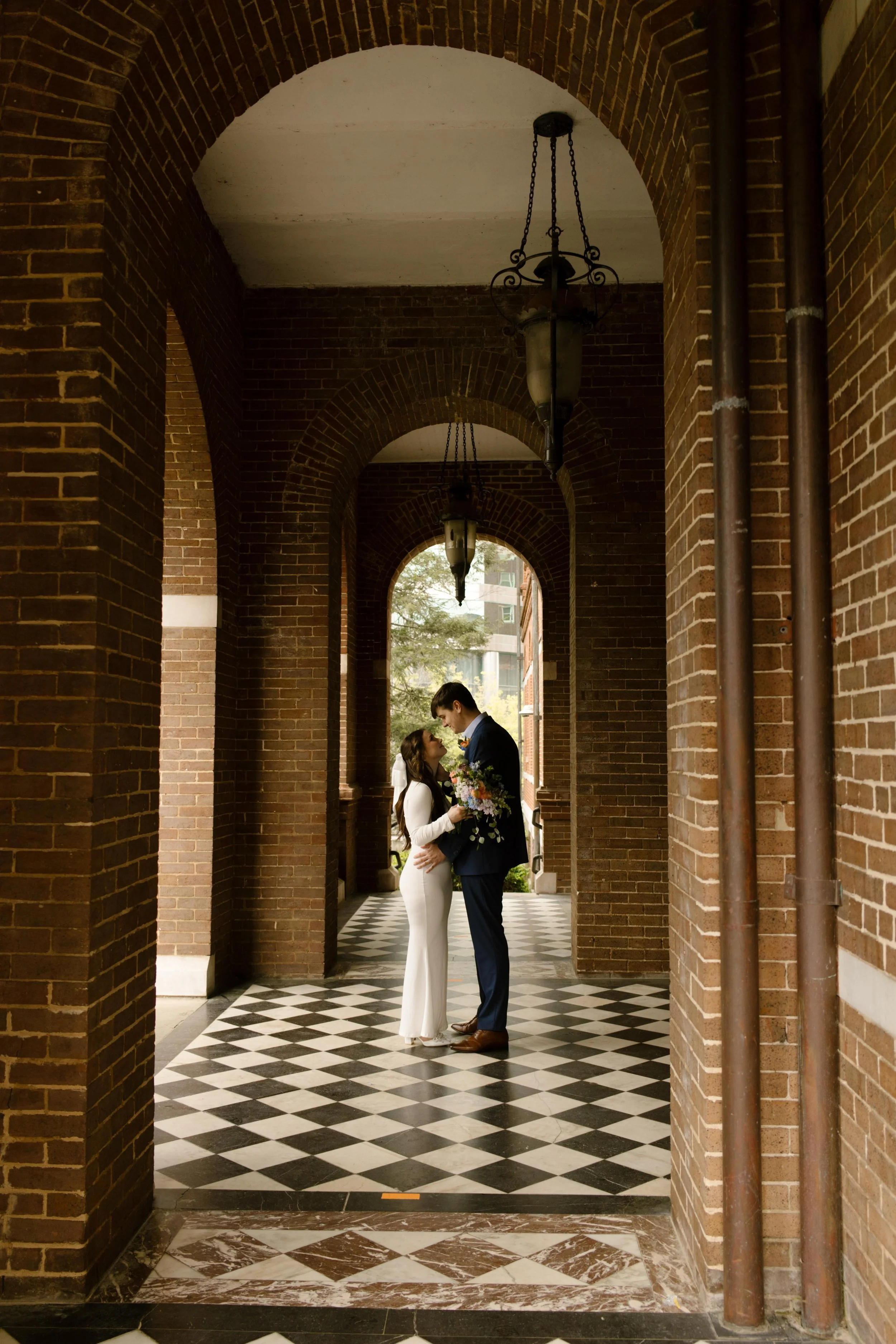 The couple shares an intimate kiss under the grand brick arches and checkerboard floors during their Knoxville courthouse elopement.