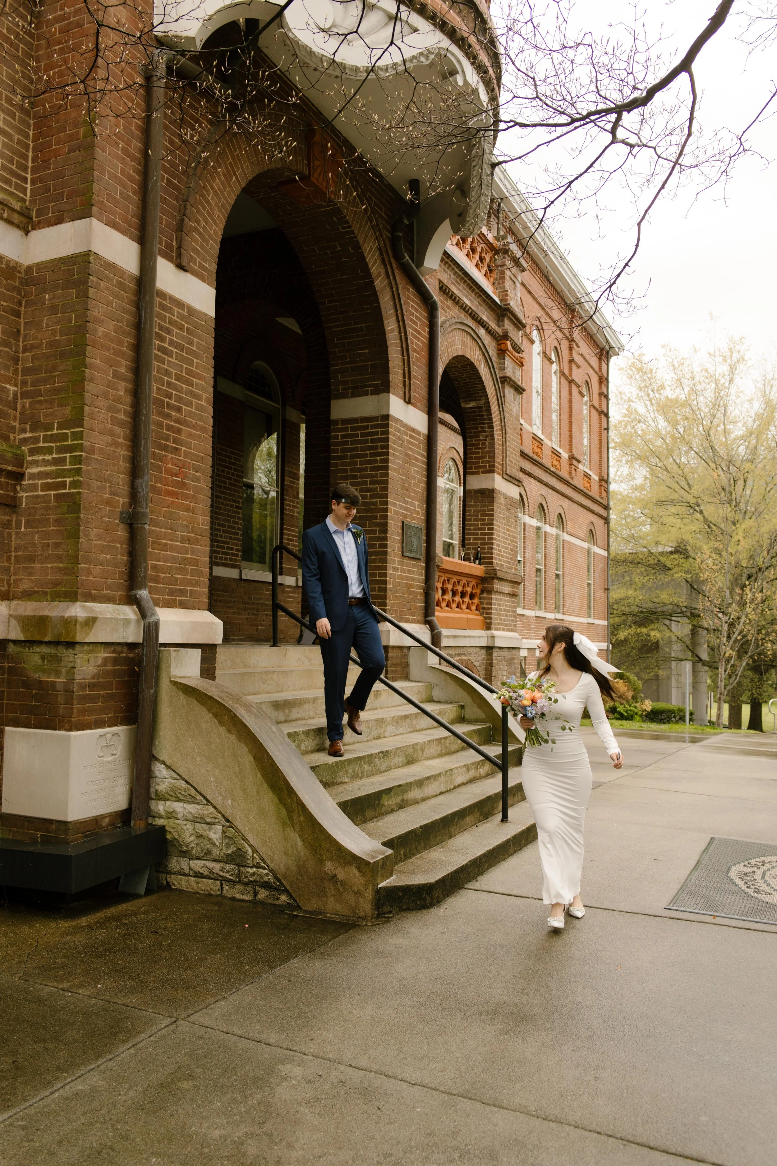 The groom descends the courthouse steps while the bride, bouquet in hand, runs up to meet him—capturing the excitement of their wedding day.