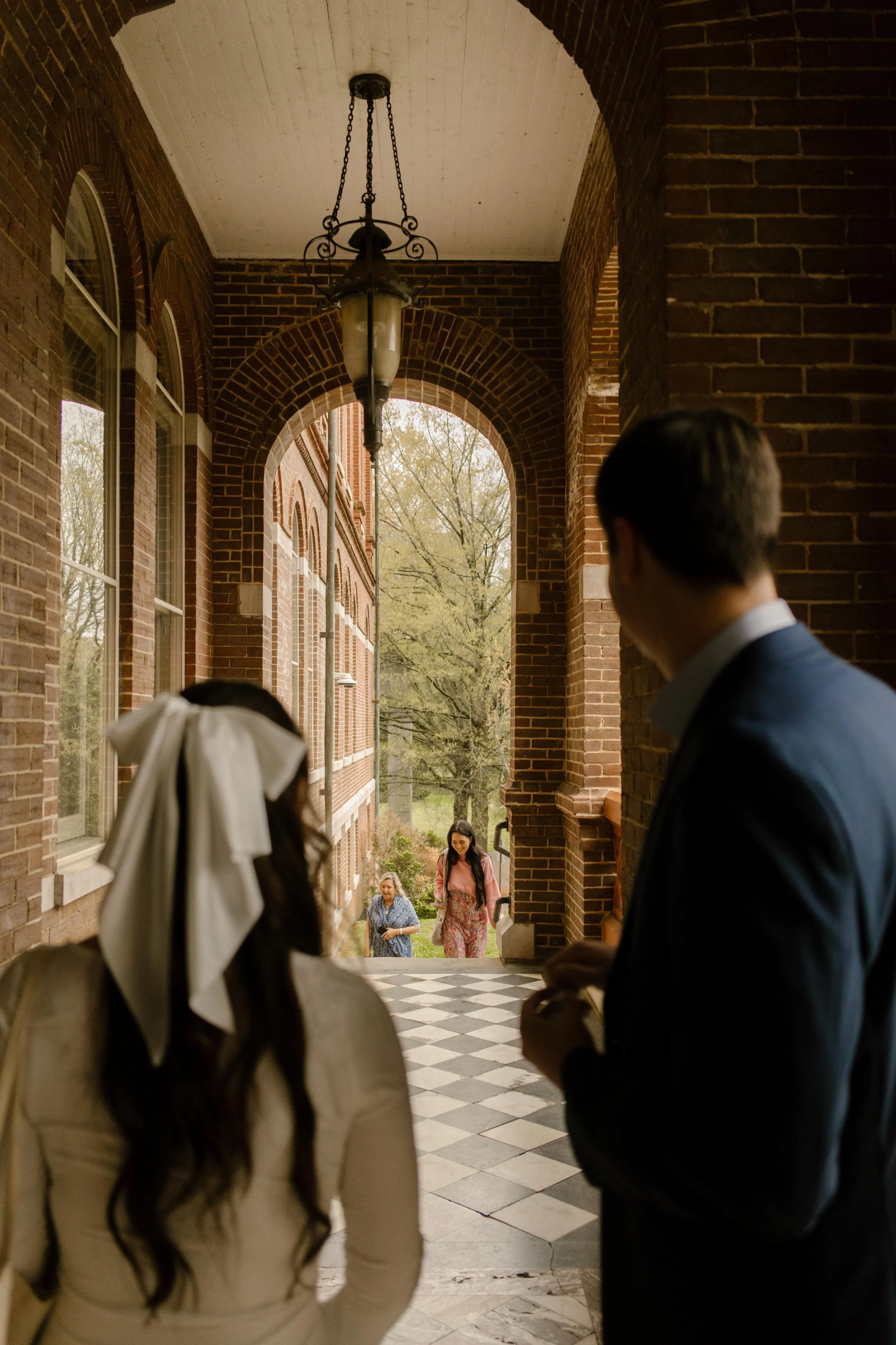 The couple watches guests approach through the brick archway, anticipation building as the ceremony nears.