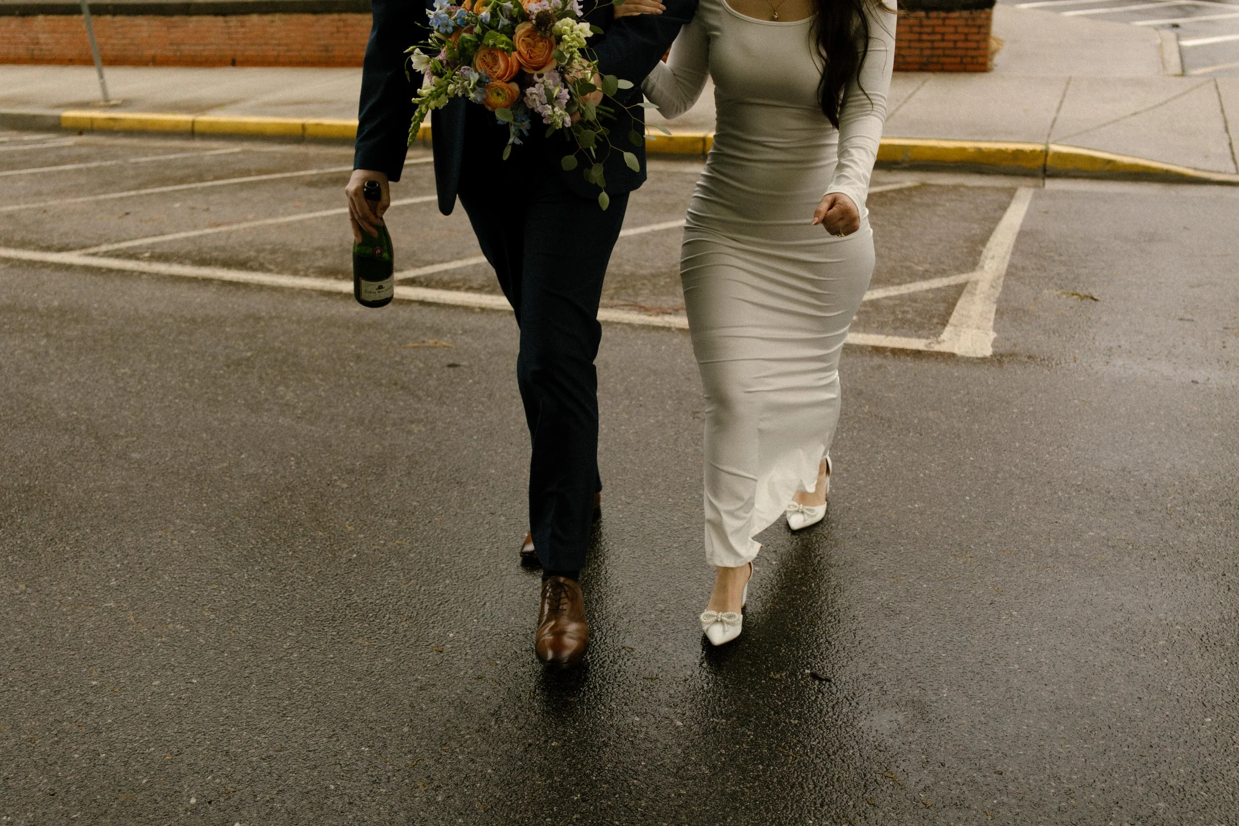 A joyful moment as the newlyweds run hand-in-hand through the parking lot, bouquet and champagne bottle in tow after their Knoxville courthouse elopement.