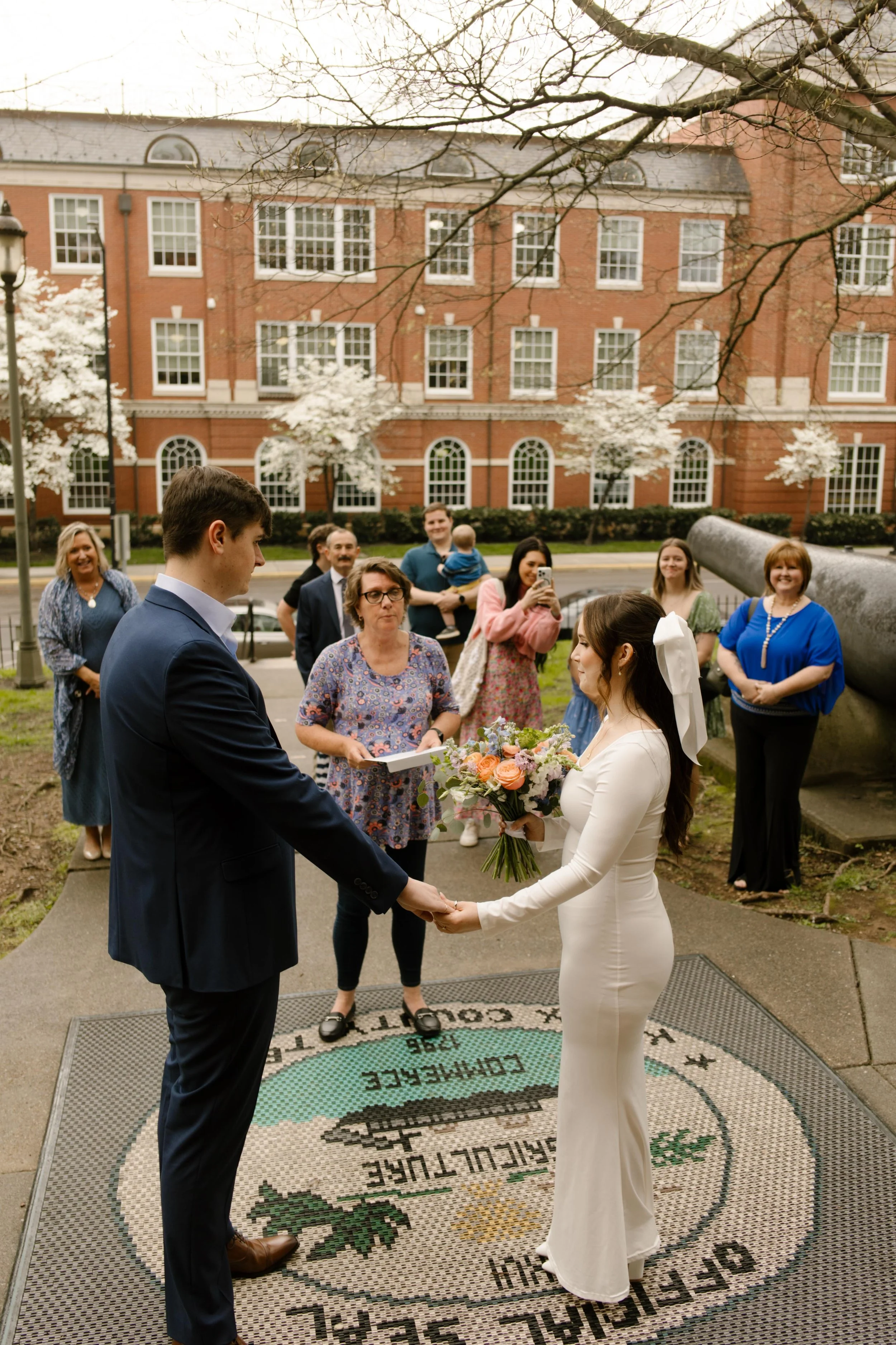 The couple holds hands during their outdoor ceremony as friends and family gather around—joyful moments from their Knoxville courthouse elopement.