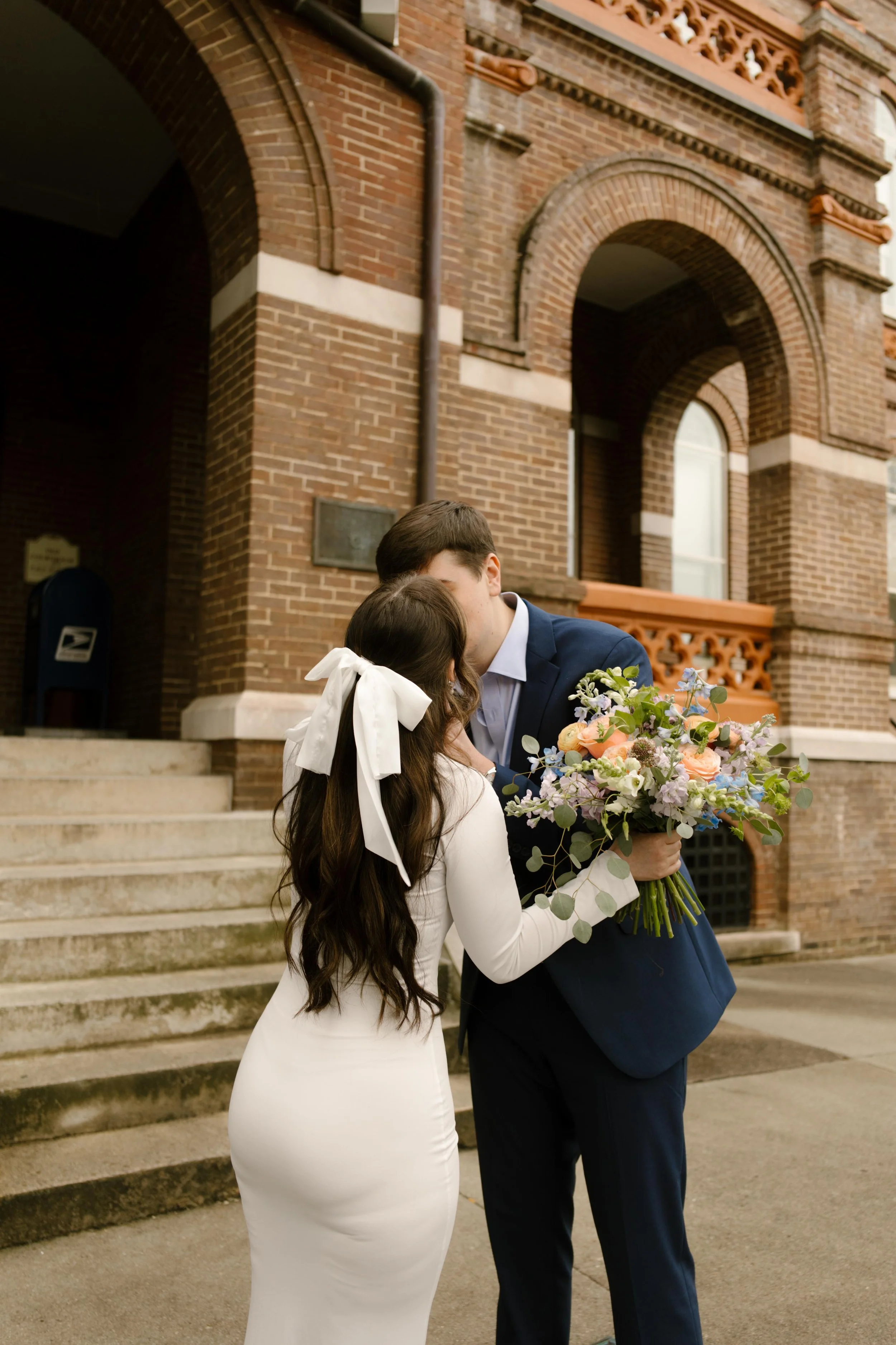 A sweet kiss on the courthouse steps, the bride’s white bow and bouquet front and center—part of their Knoxville courthouse elopement celebration.