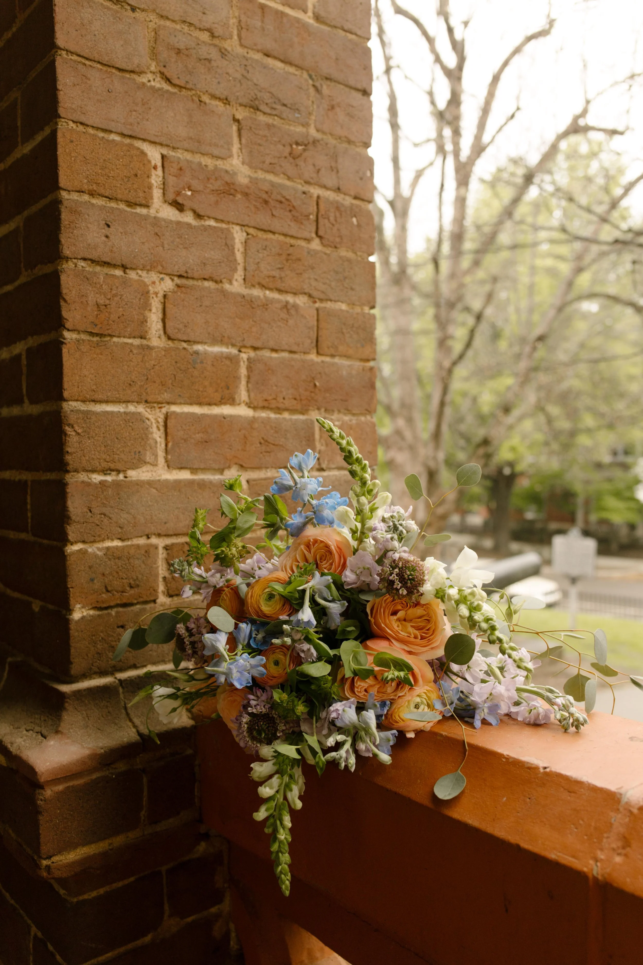 A colorful spring bouquet with orange ranunculus and soft blue delphinium rests on a brick ledge at the Knoxville courthouse.