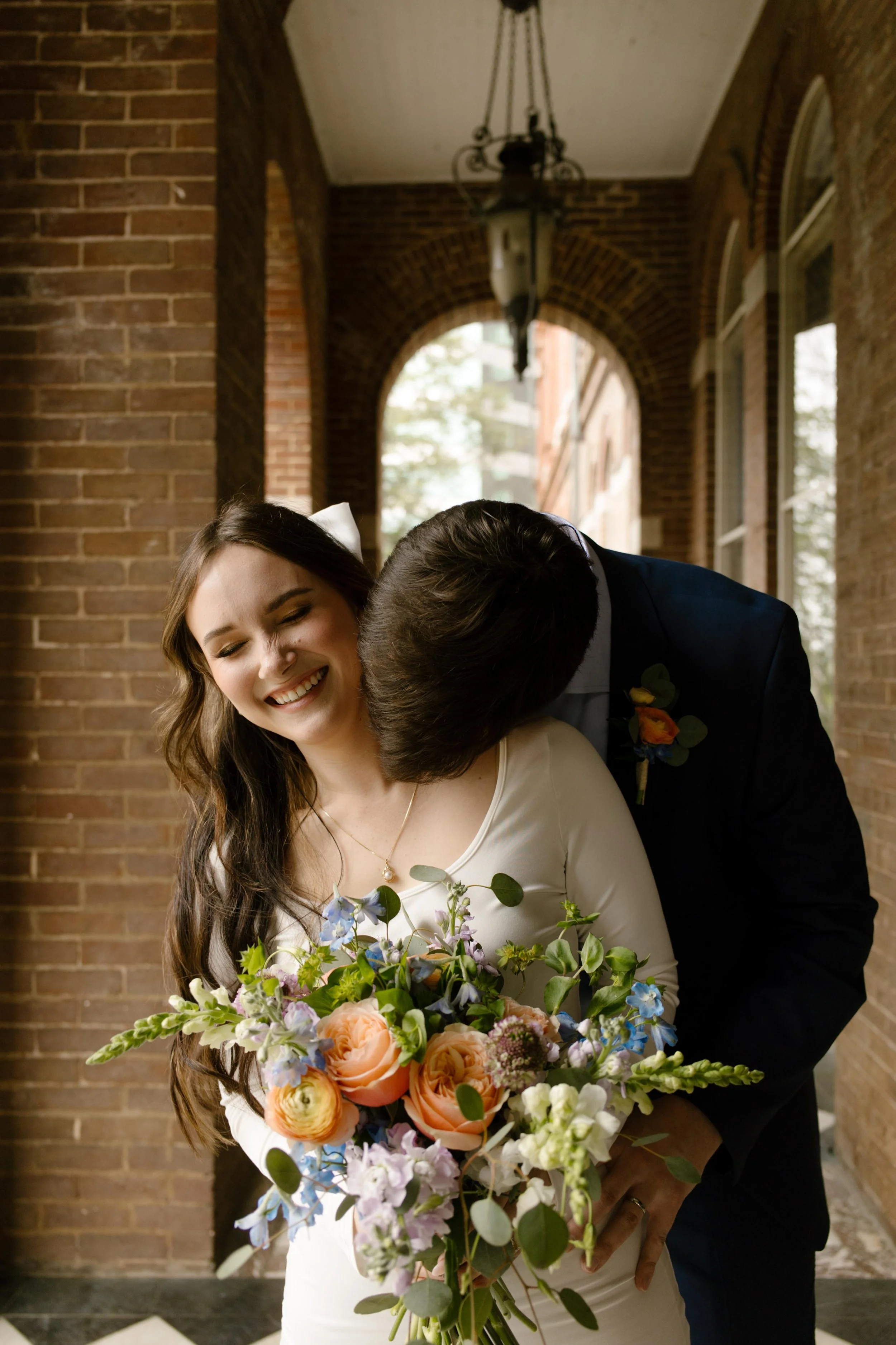 Bride laughs as the groom kisses her shoulder from behind, bouquet in hand and joy radiating after their Knoxville courthouse elopement.