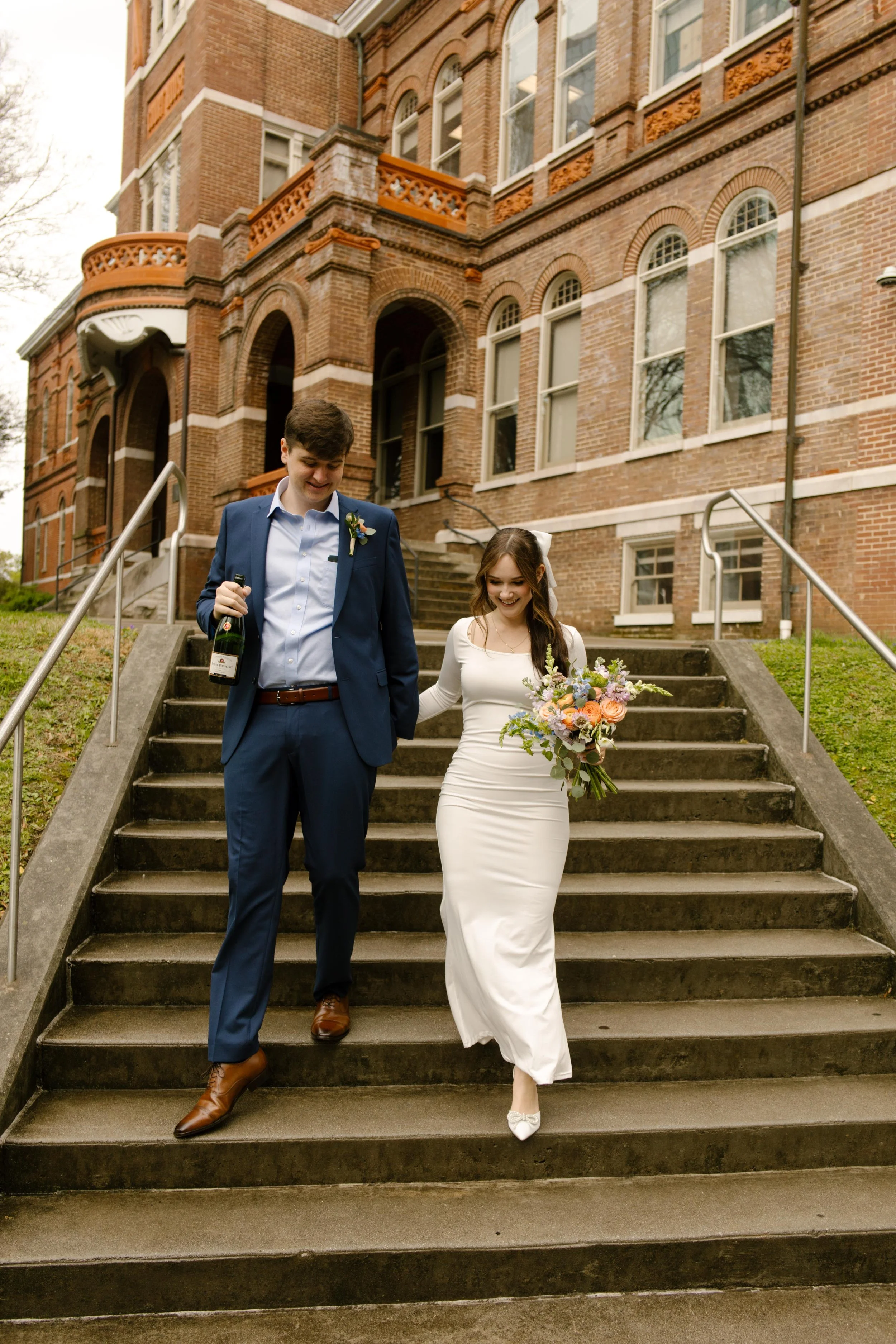 Newly married and beaming, the couple walks down the courthouse steps—champagne in hand, love in full swing after their Knoxville courthouse elopement.
