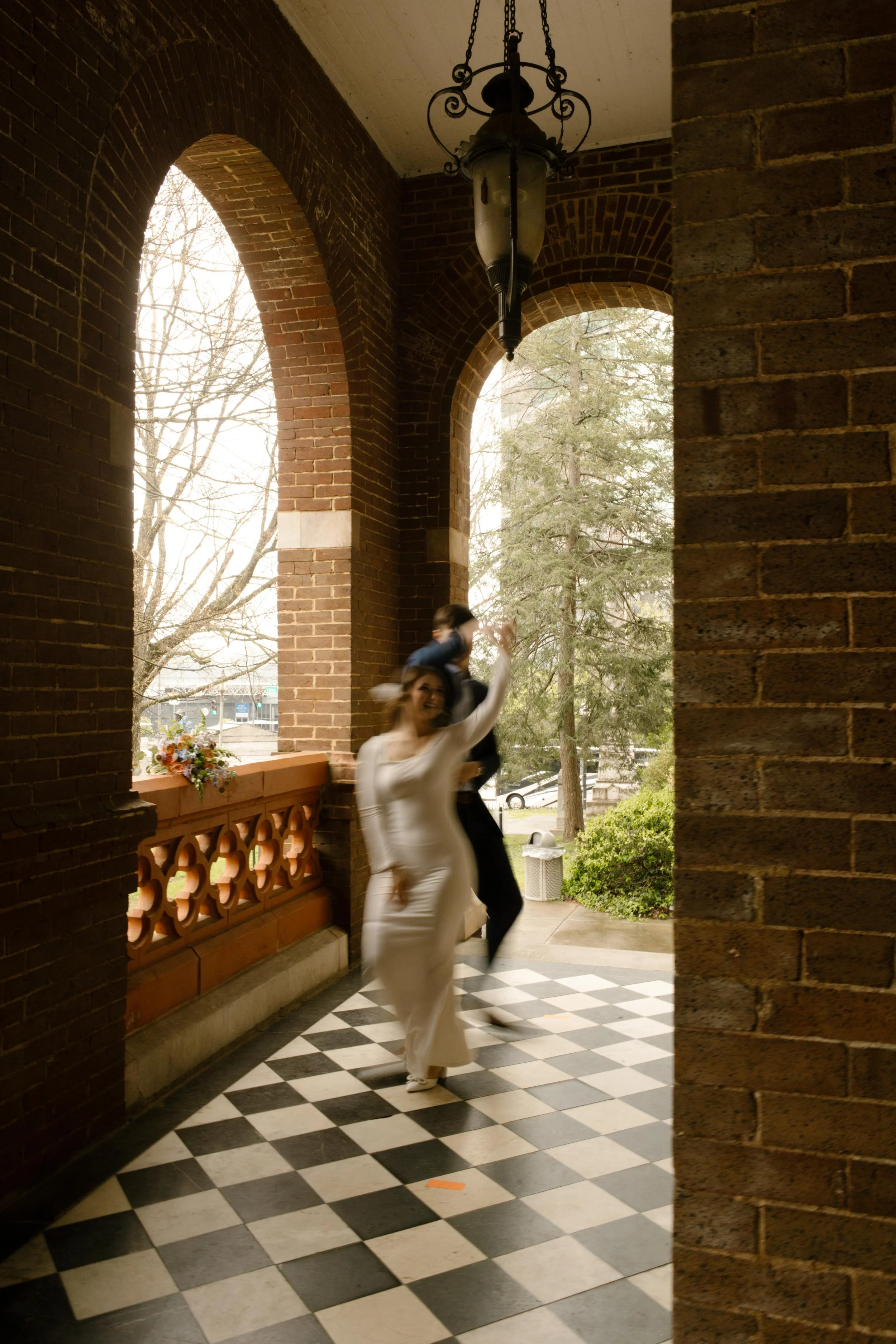 A motion-blur moment of the couple dancing down the black-and-white tiled corridor of the courthouse, full of joy and just-married energy.