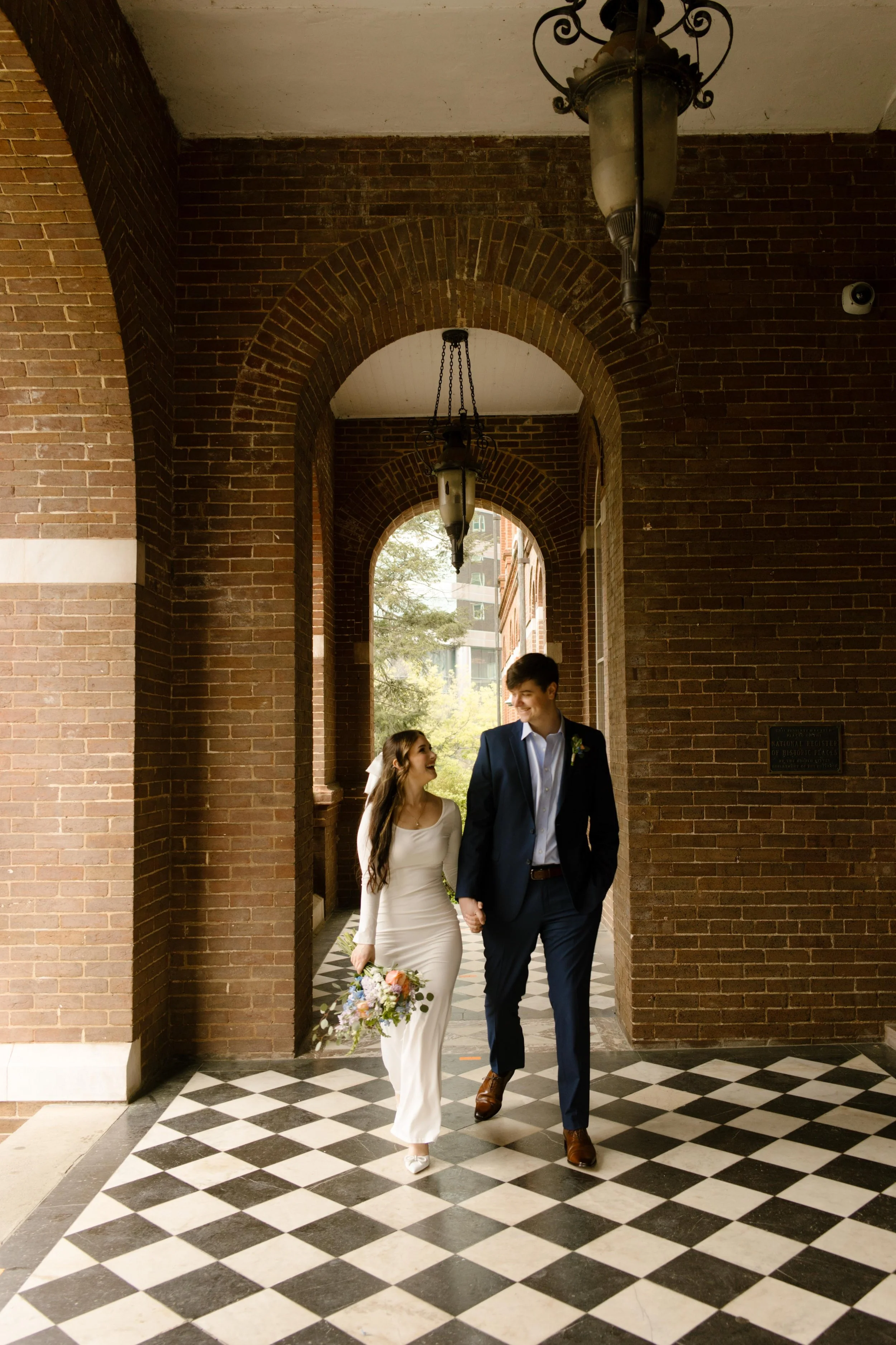 Hand in hand, the couple walks confidently through the brick archway of the courthouse, bouquet in one hand, love in the other.