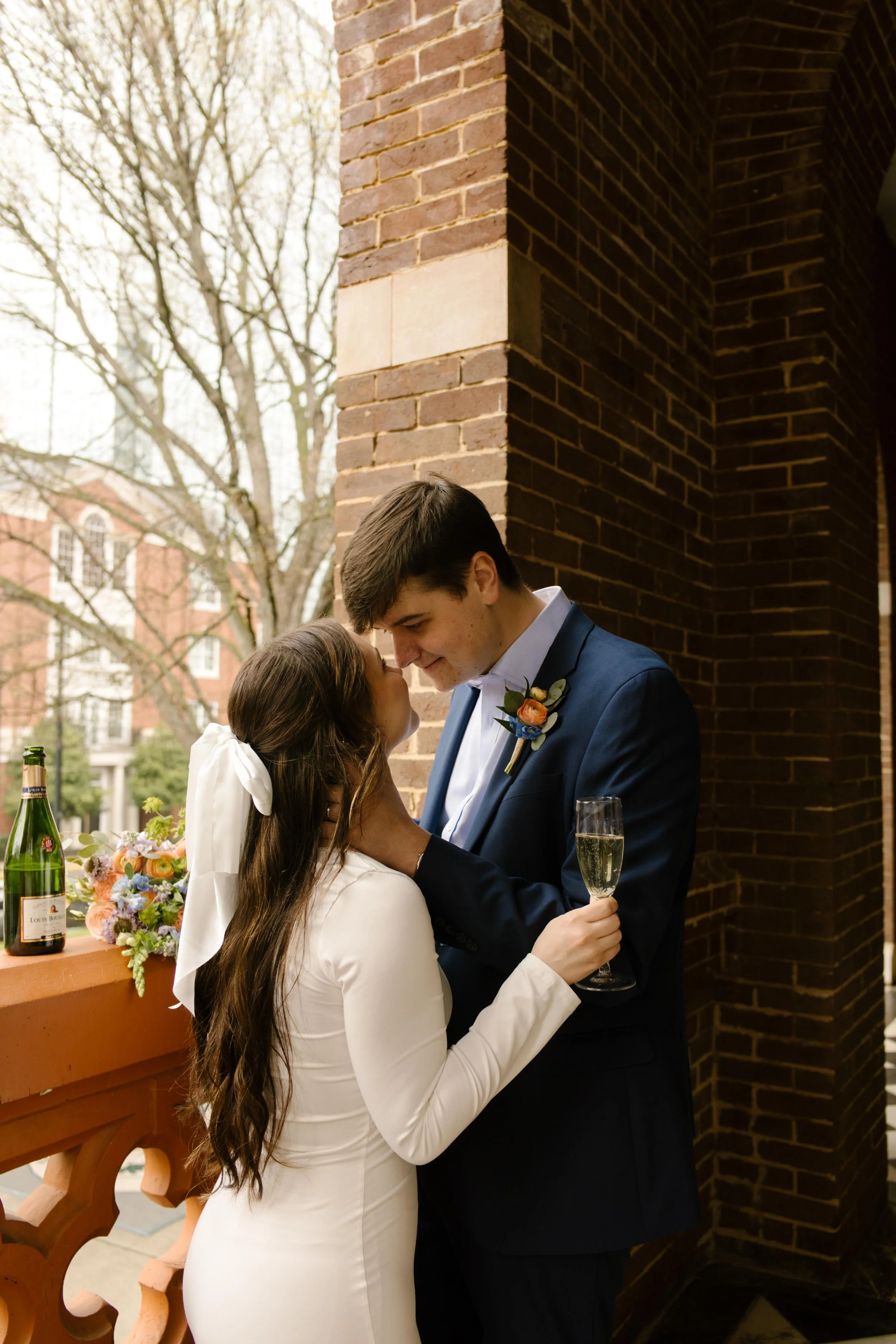 The couple shares a champagne toast and a quiet, forehead-to-forehead moment on the courthouse balcony, celebrating just after saying “I do.”