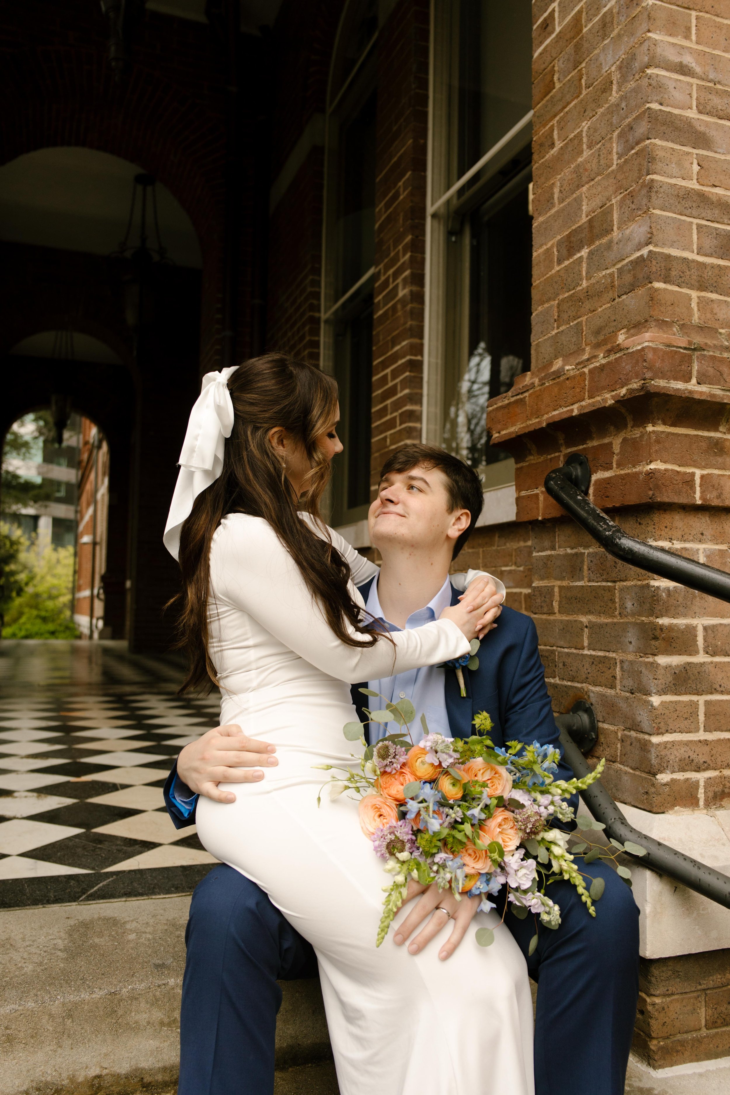Knoxville courthouse elopement moment: bride sits on the groom’s lap on the front steps, both wrapped in laughter and wildflower-colored blooms.