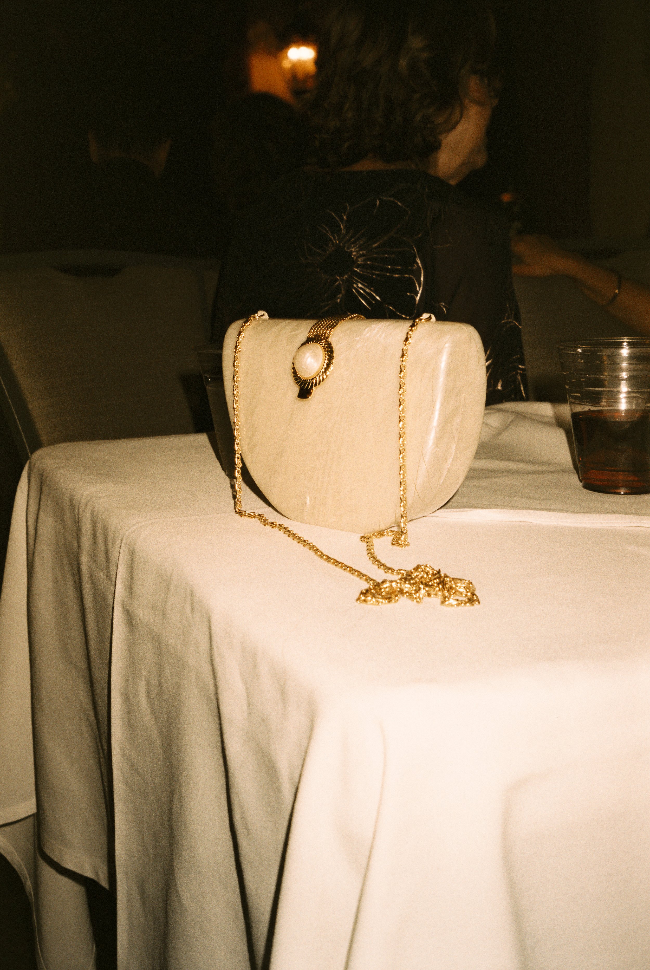 A vintage-inspired clutch resting on a reception table, surrounded by soft light and a drink left mid-conversation.