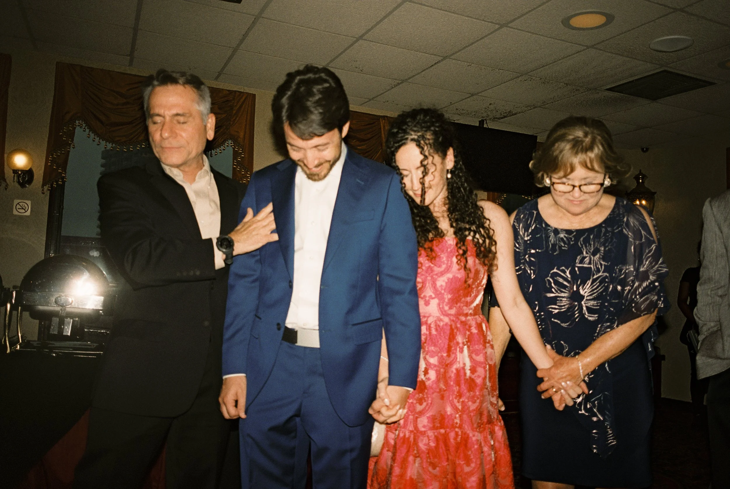 The couple holding hands with their parents in an emotional moment at their wedding welcome dinner.