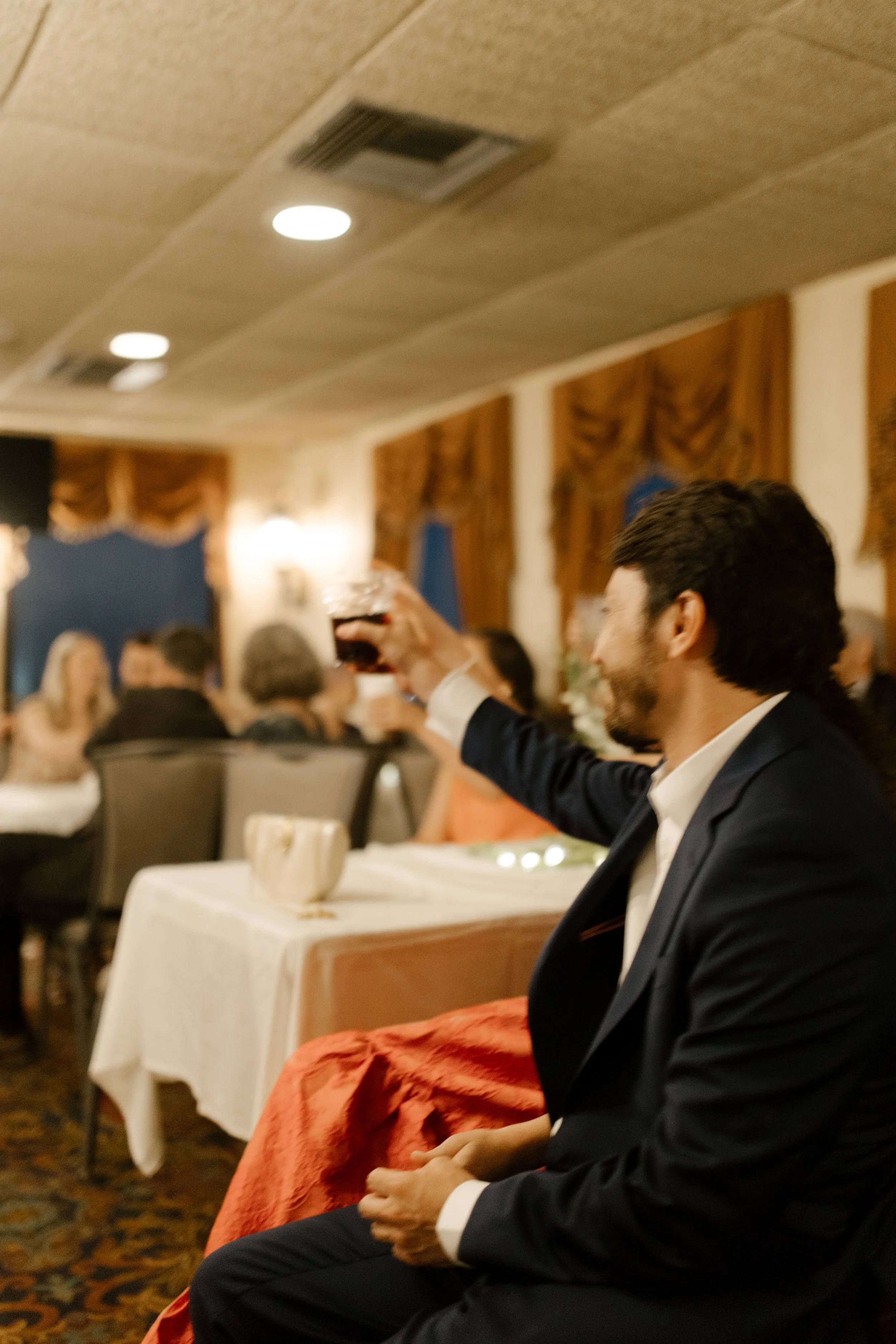 The groom raises a glass for a toast, celebrating among friends and family during the wedding dinner cruise.