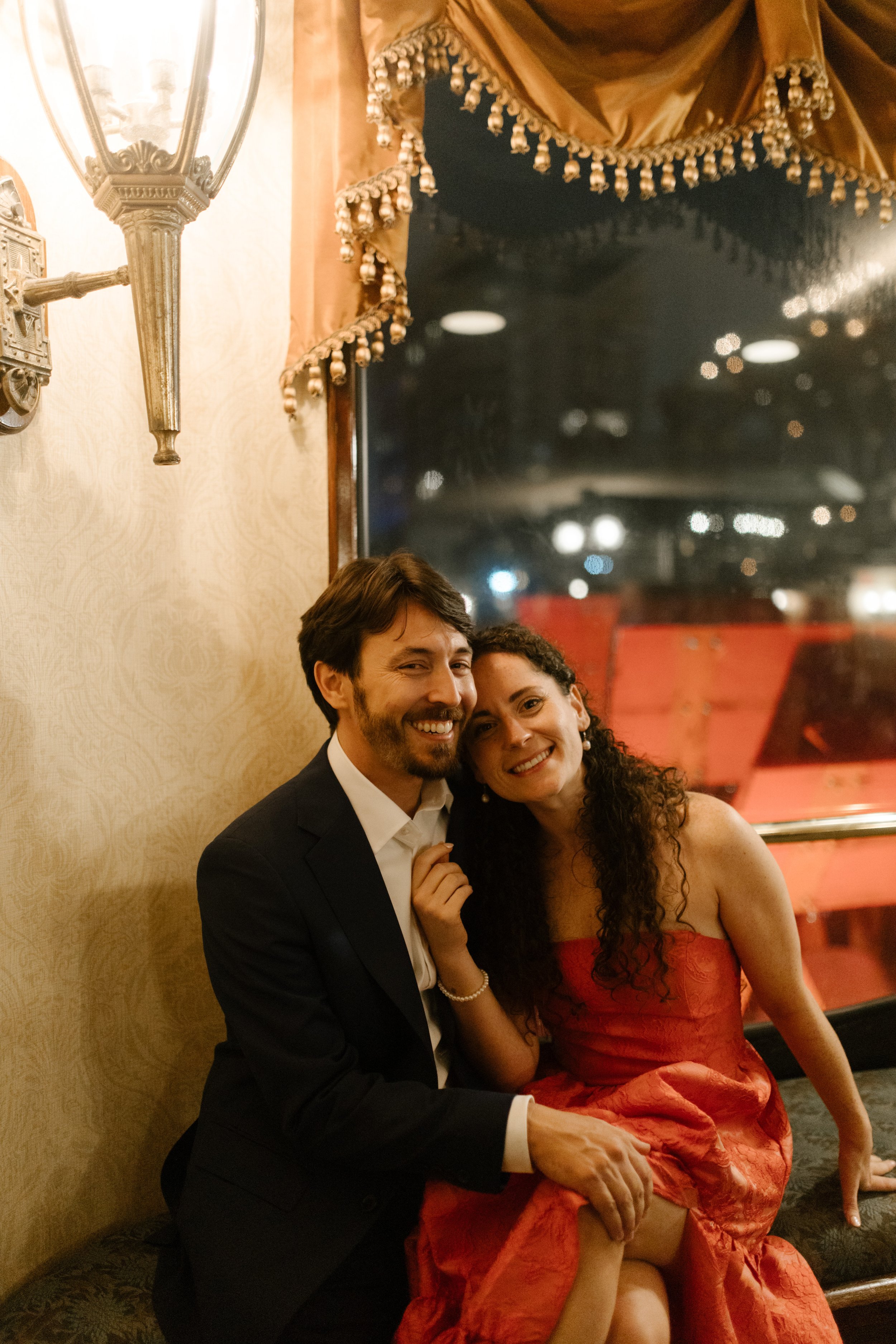 Bride leans into her groom smiling full of joy while looking out the dark window during their night cruise on Creole Queen.